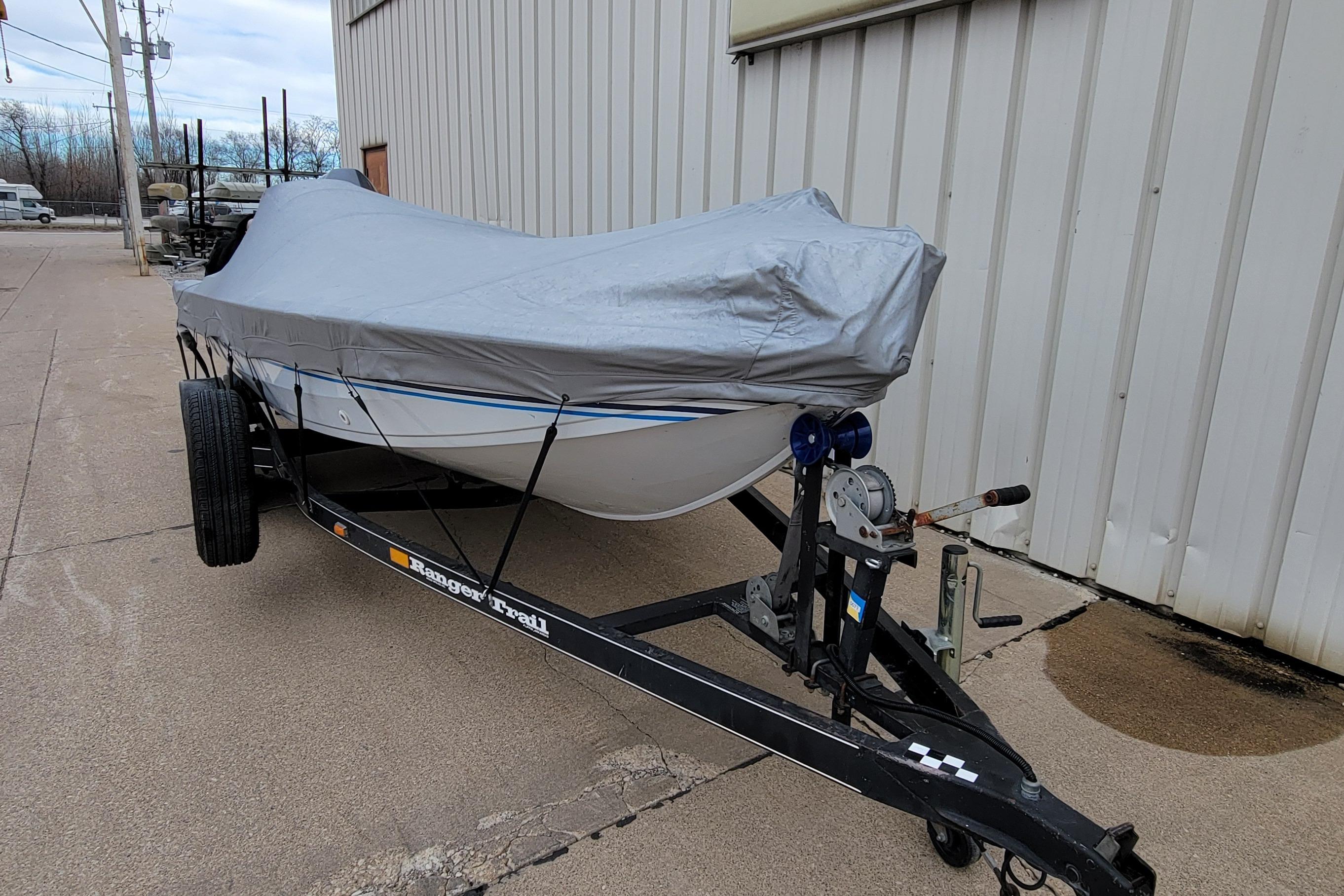 1999 Ranger 107 Cherokee boat covered on trailer near building.