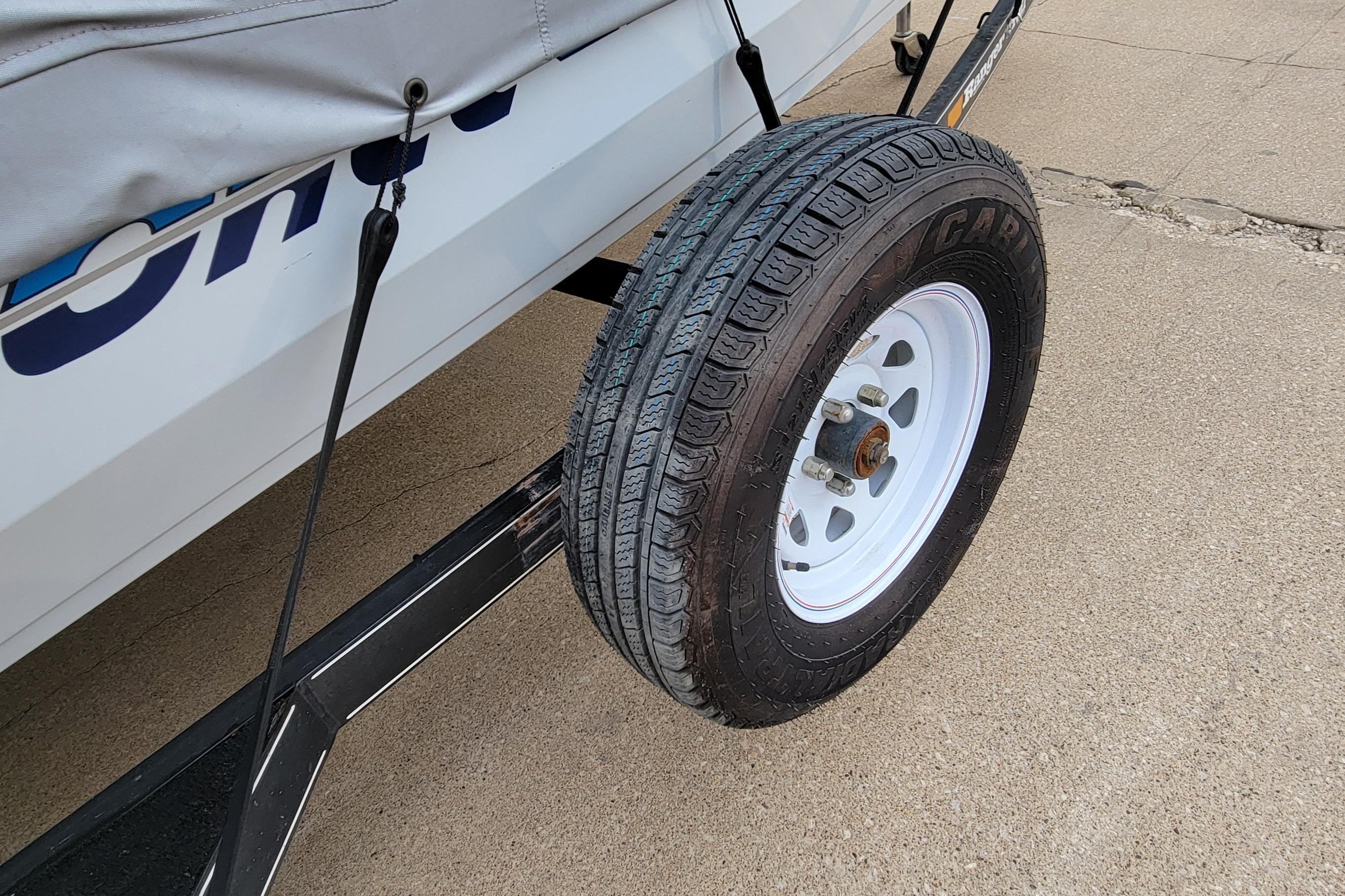 Trailer tire on a 1999 Ranger 107 Cherokee boat trailer, parked on concrete.