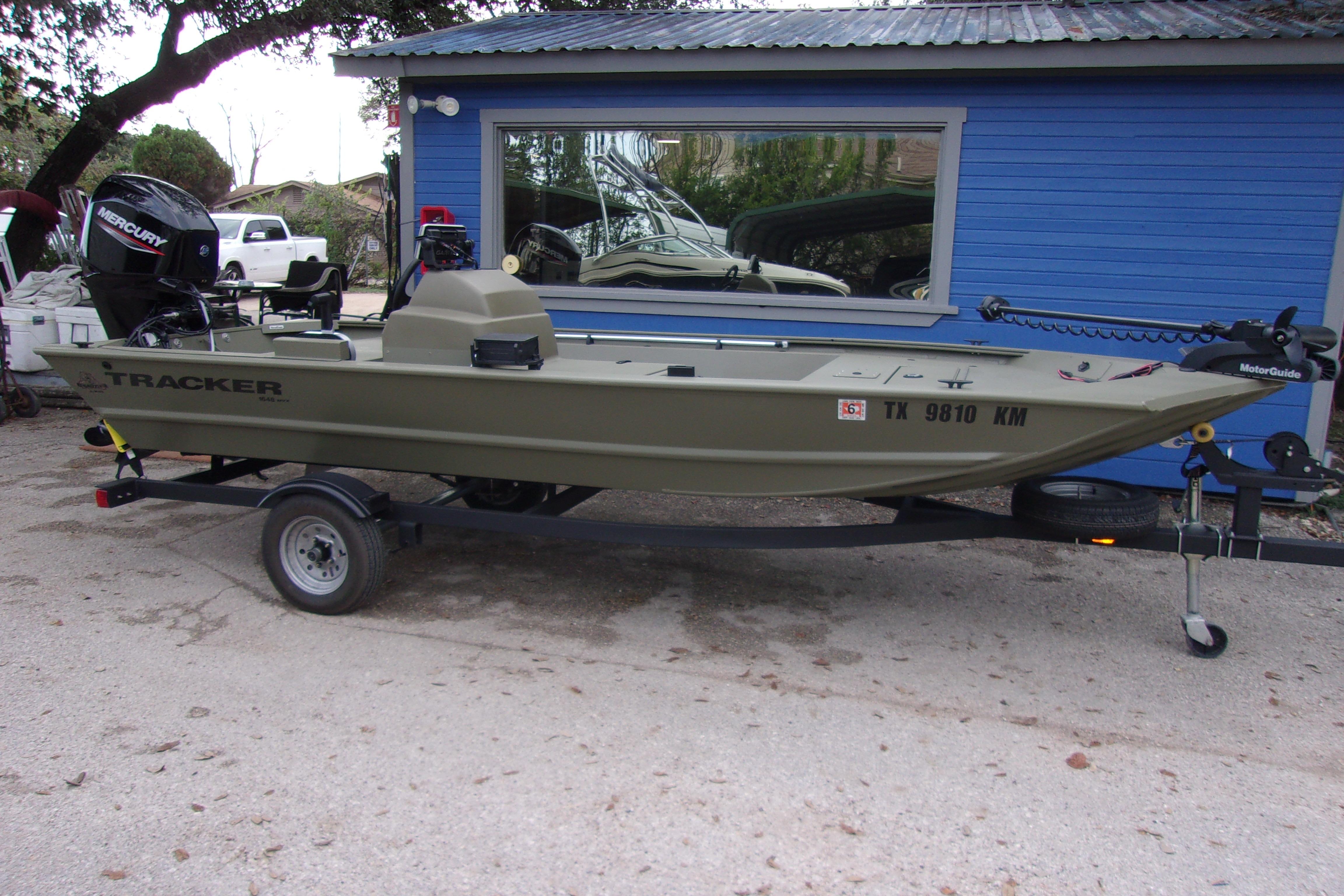 2022 Tracker Grizzly 1648 MVX SC boat on trailer, parked by blue building.