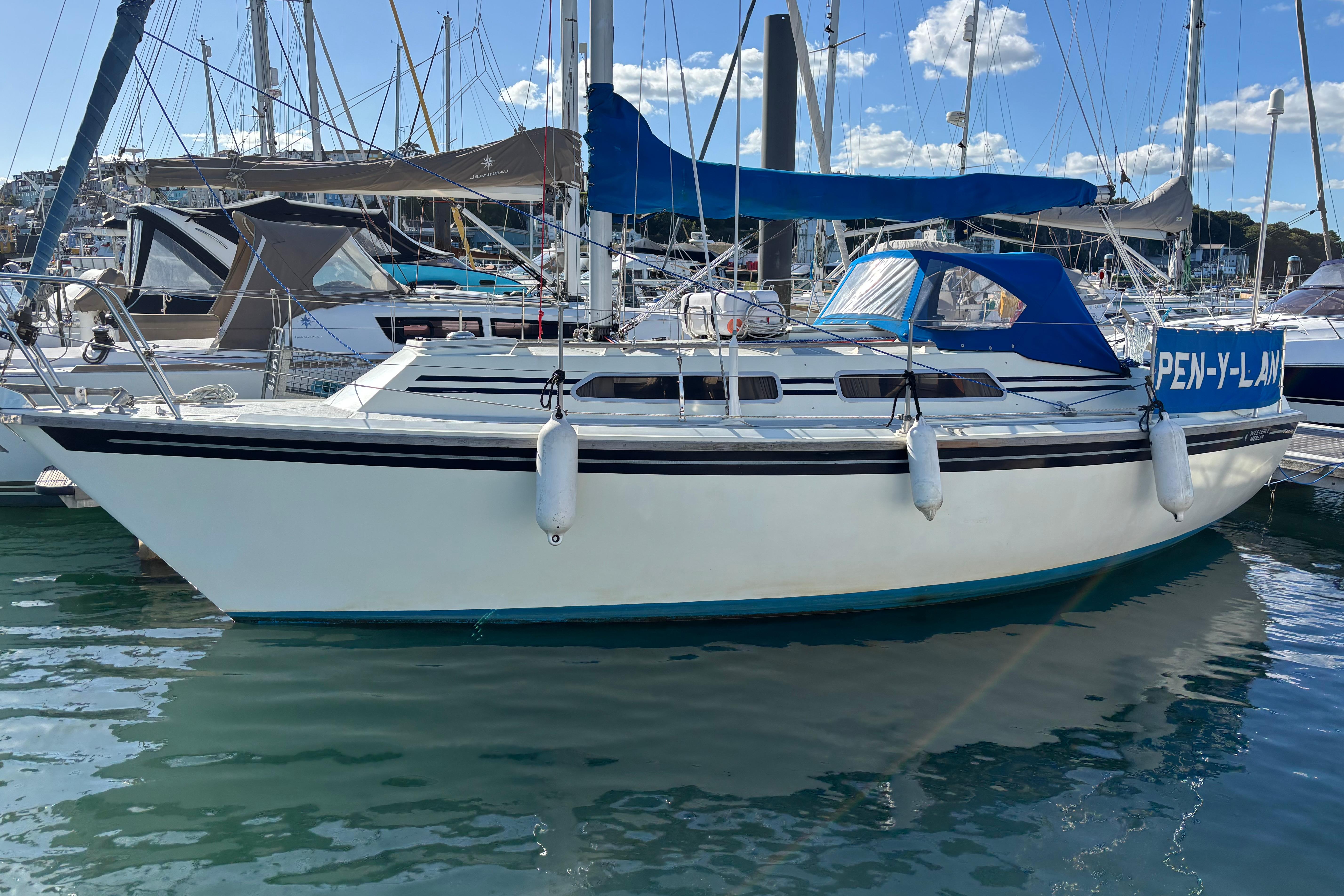1986 Westerly Merlin sailboat docked in marina, blue canopy, calm water, clear sky.