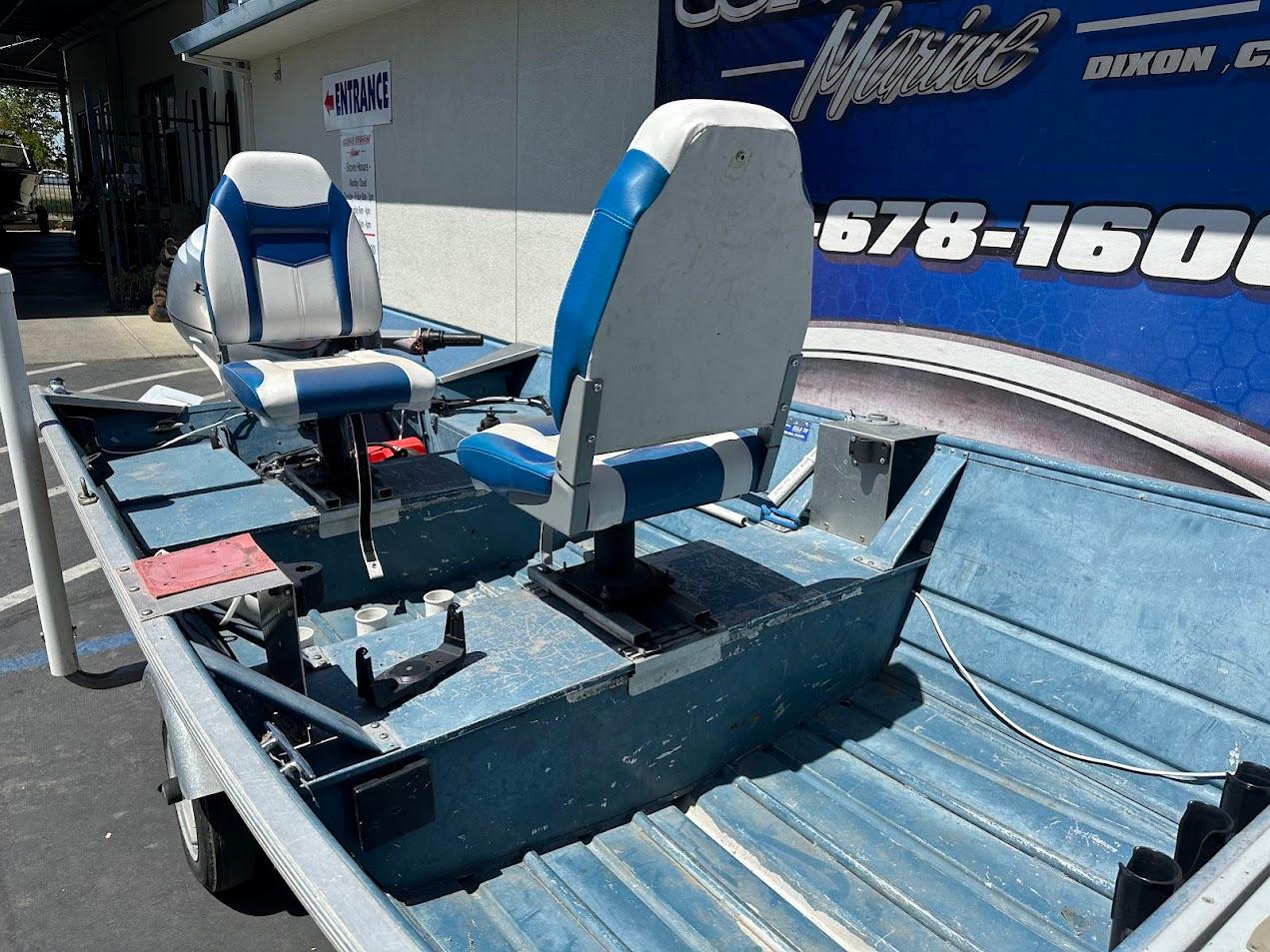 1998 Klamath 14 DLX boat with blue and white seats, parked outside a marine shop.