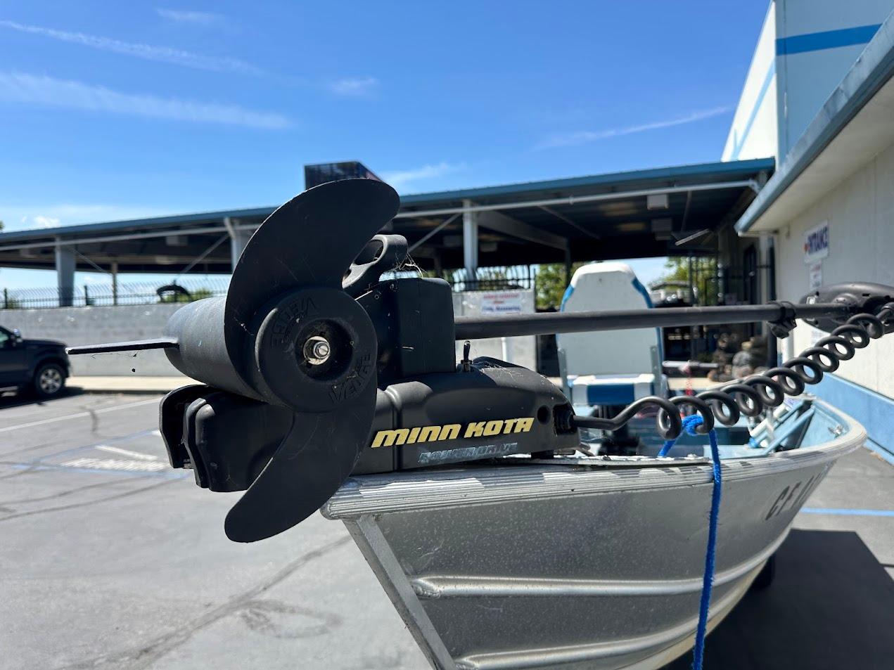 1998 Klamath 14 DLX boat with Minn Kota motor in a parking lot.