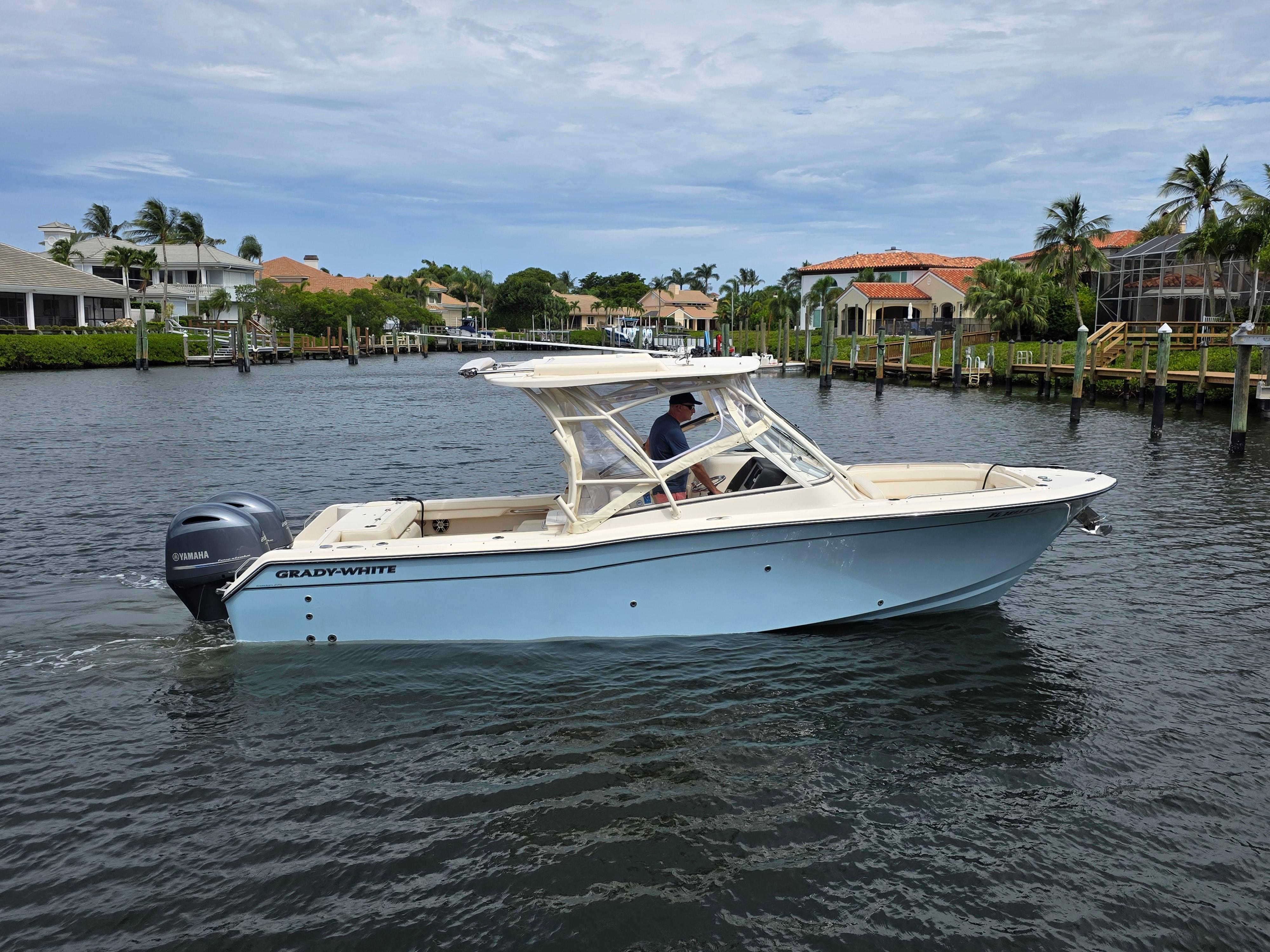 2023 Grady-White Freedom 275 boat cruising on a scenic waterfront with luxury homes.