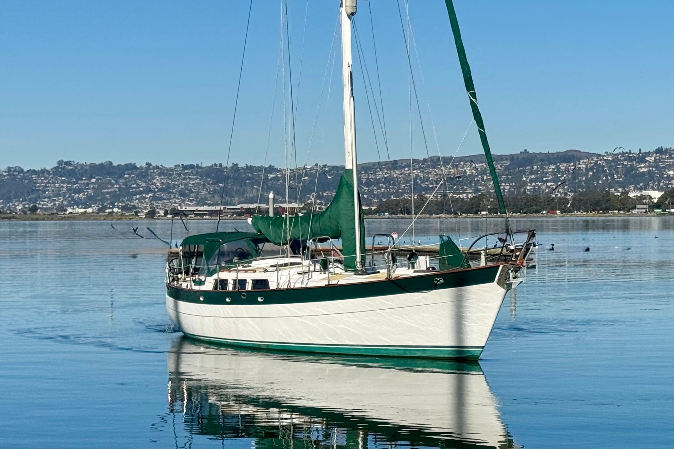 Sailboat "Christina" by Hans Christian, 1988, on calm water with scenic background.