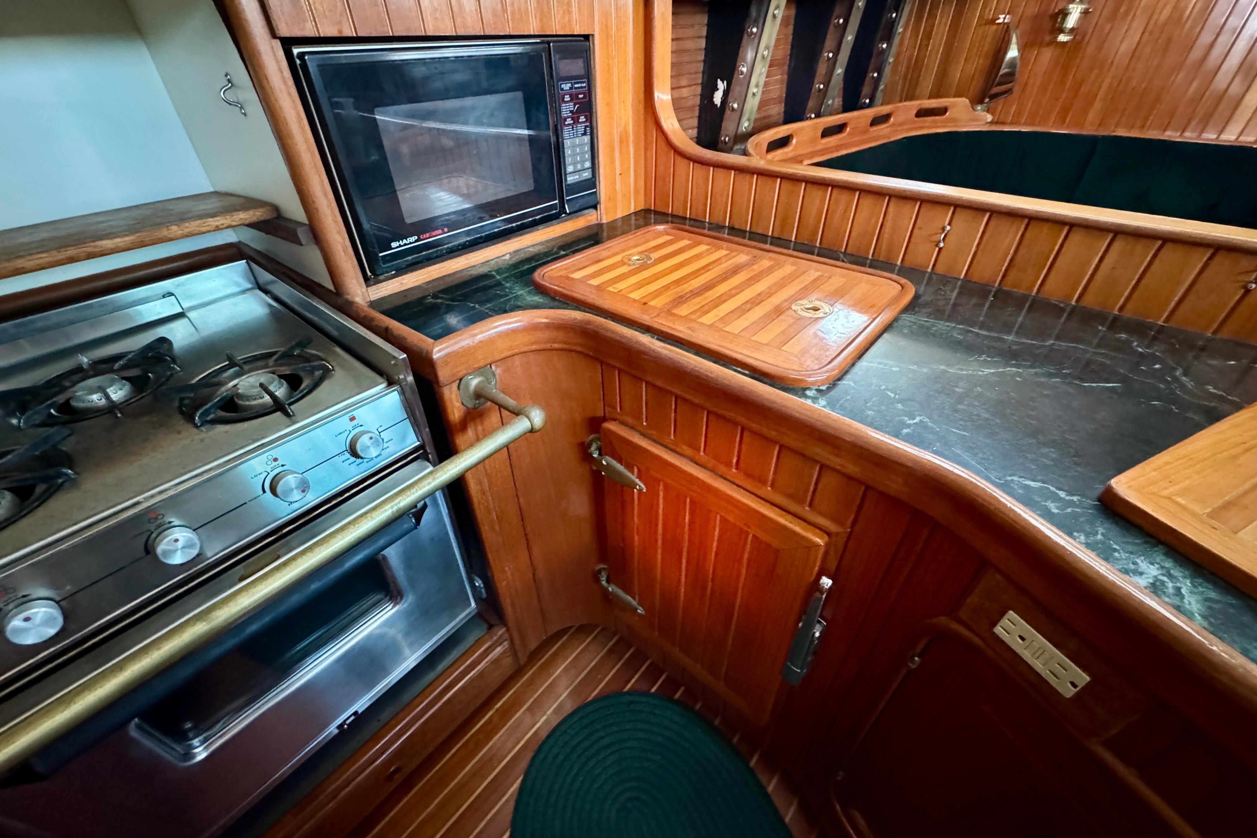 Galley kitchen in 1988 Hans Christian Christina yacht with stove, microwave, and wooden cabinetry.