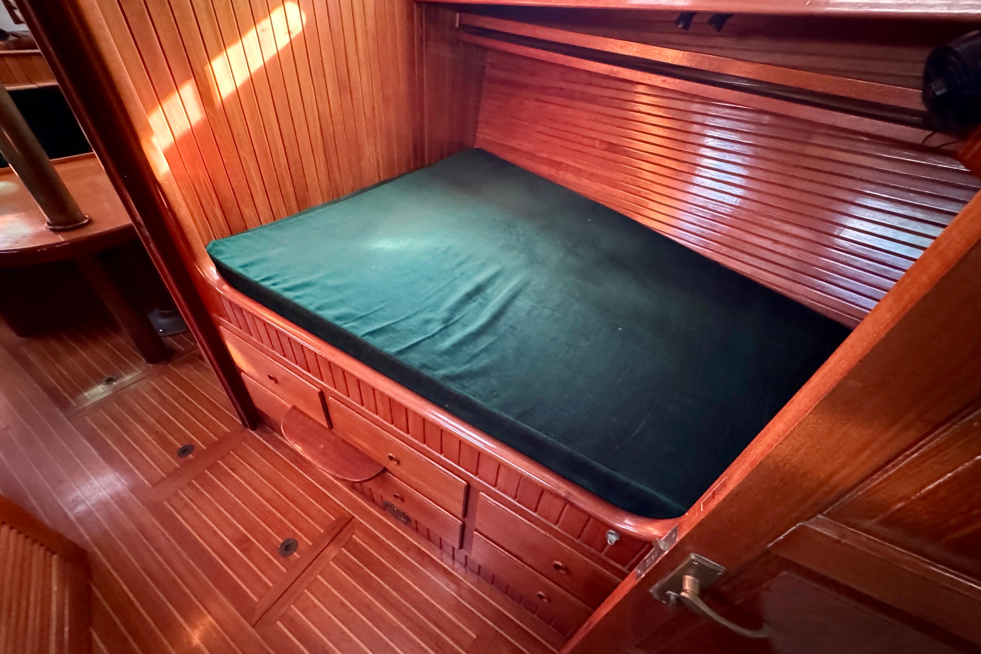 1988 Hans Christian Christina cabin interior with wooden paneling and green cushioned berth.