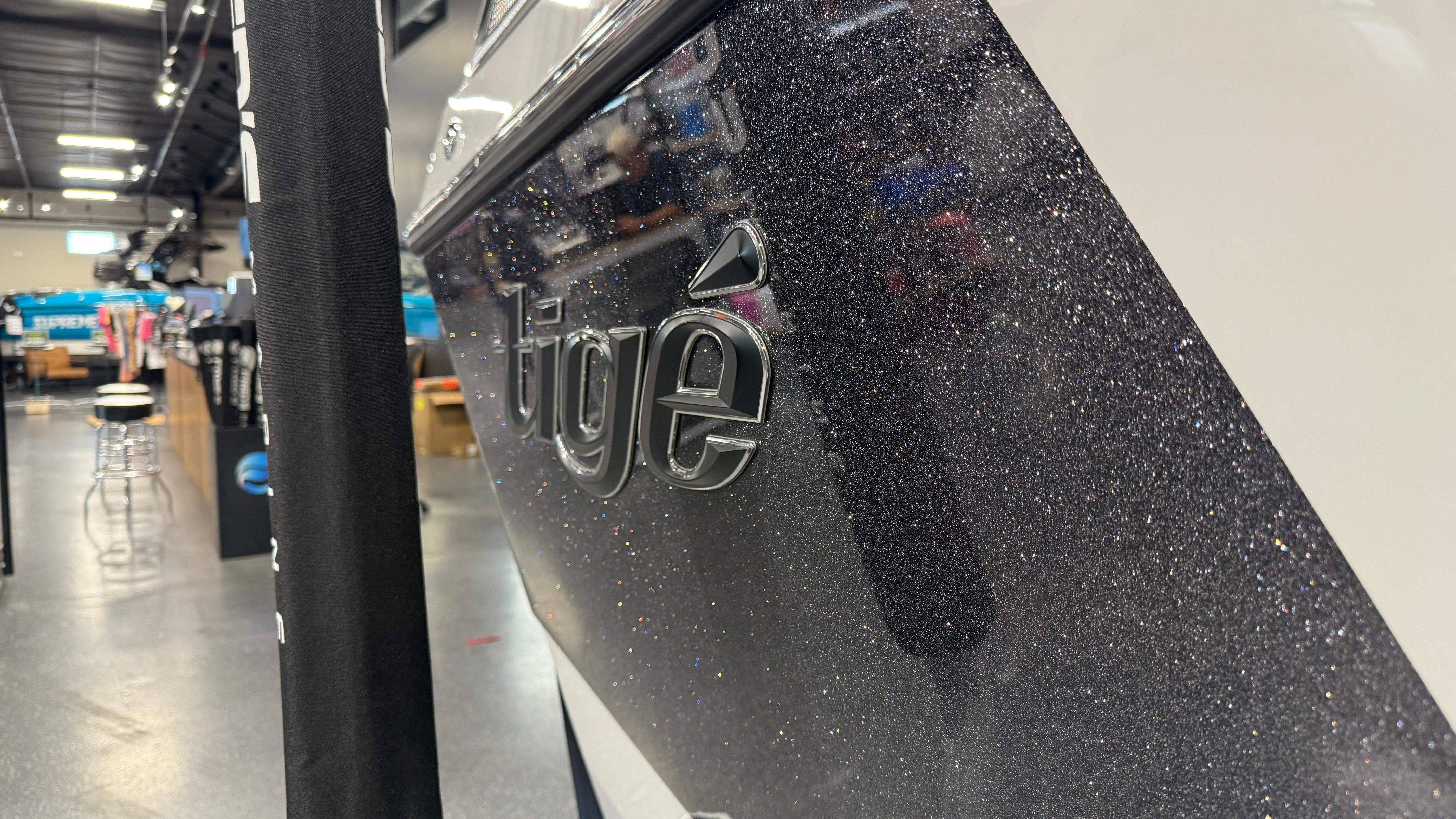 2022 Tigé 23ZX boat in showroom, close-up of logo on sleek, glittery hull.
