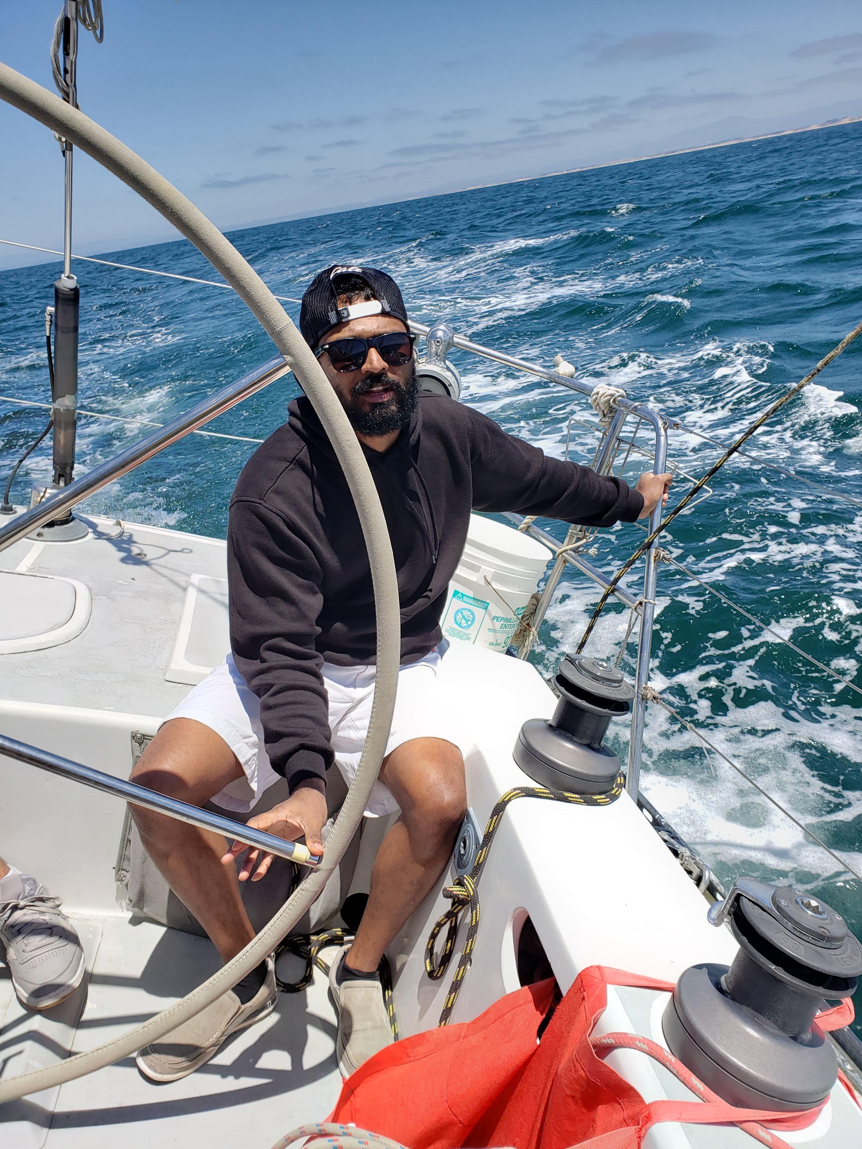 Man steering 1986 Santa Cruz 50 sailboat on open sea, wearing casual attire.