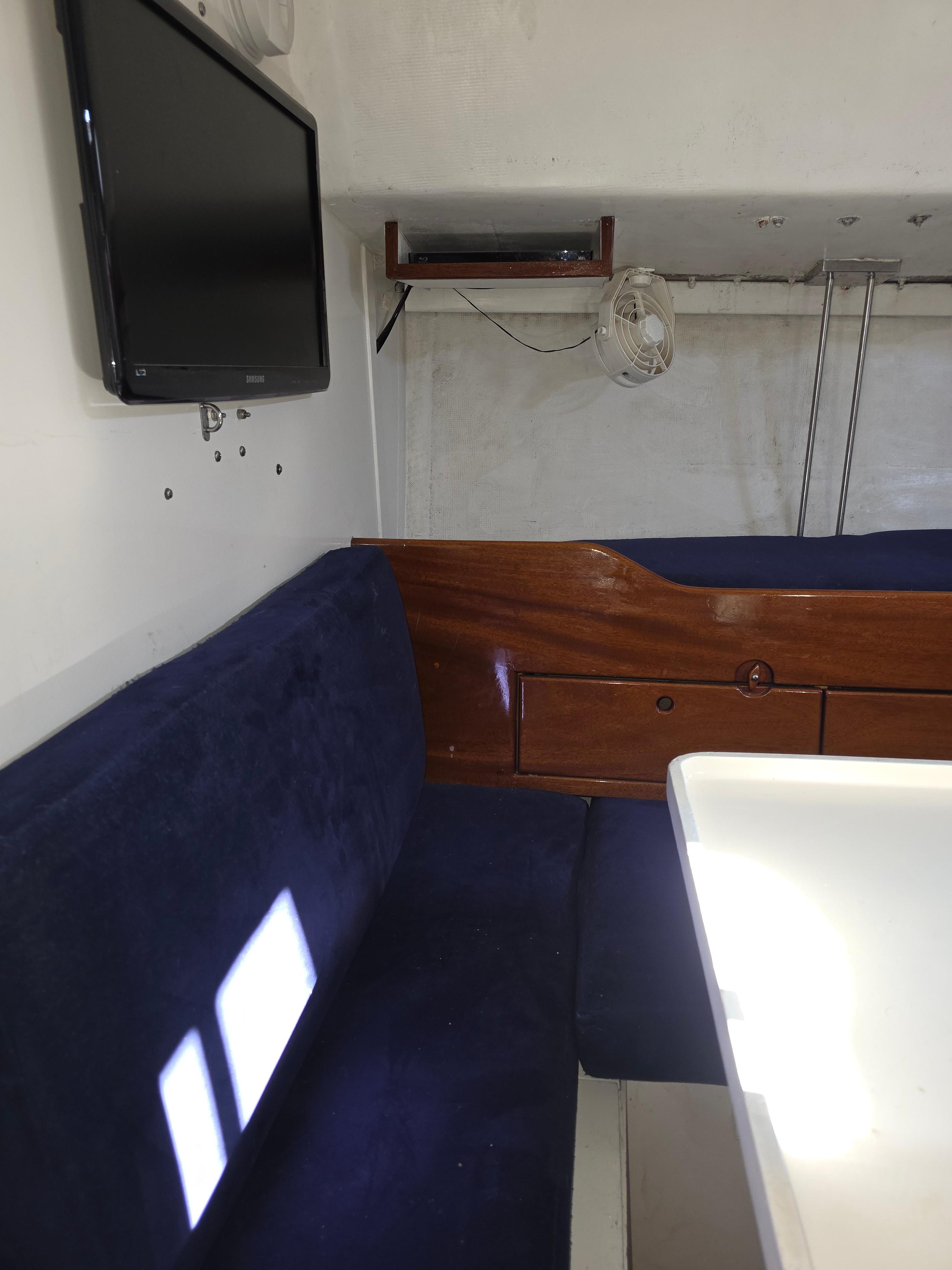 Interior of 1986 Santa Cruz 50 yacht with blue seating, wooden accents, and mounted TV.