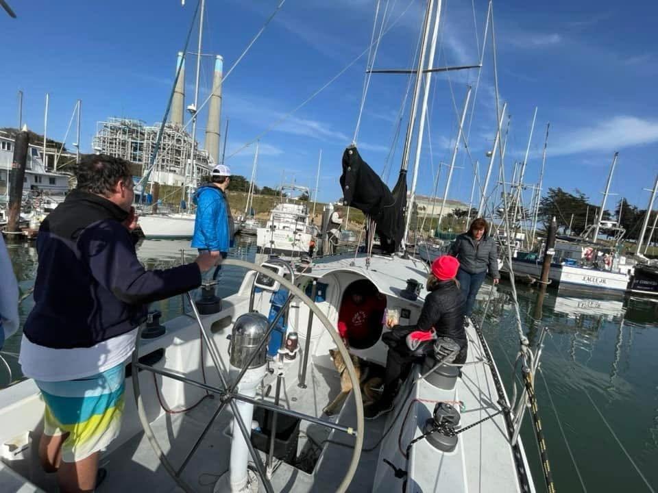 People on a 1986 Santa Cruz 50 sailboat in a marina, surrounded by other boats.
