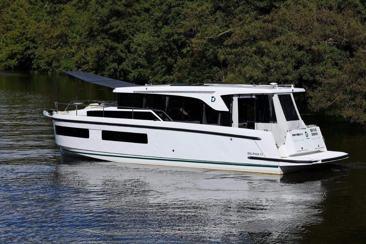 2025 Delphia D11 SEDAN boat cruising on a serene river with lush greenery.