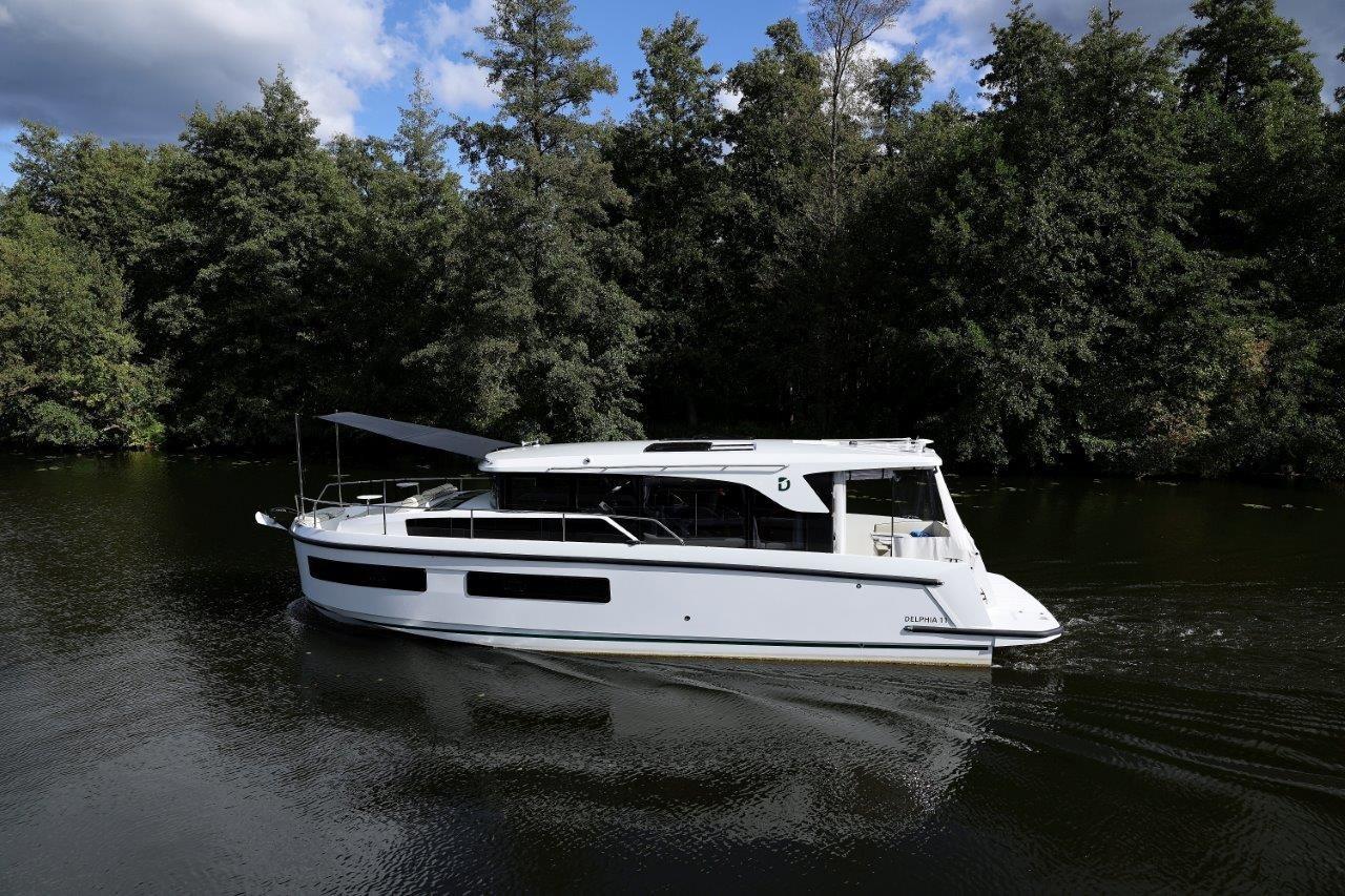 2025 Delphia D11 SEDAN cruising on a serene river, surrounded by lush greenery.