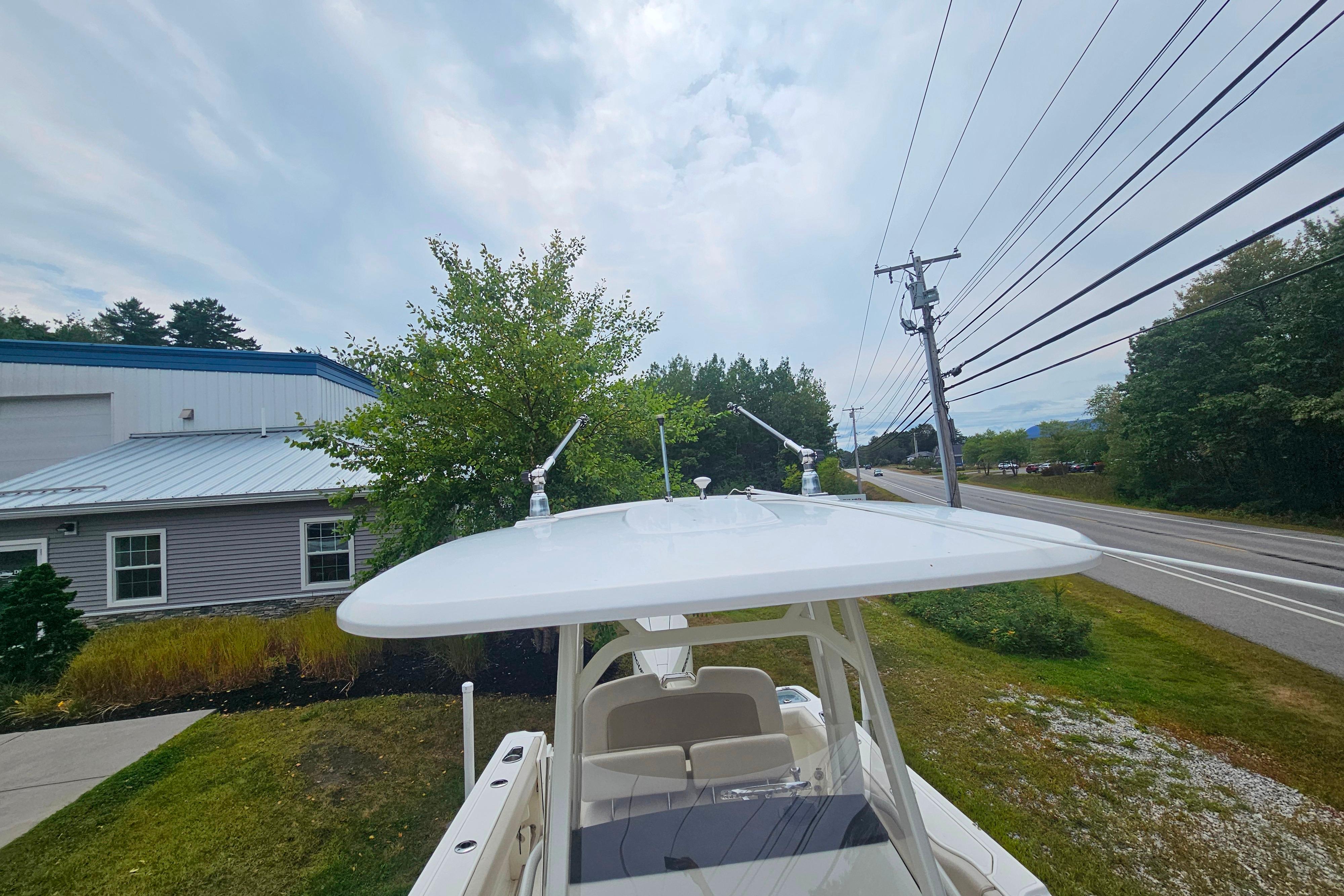 2019 Boston Whaler 230 Outrage boat with T-top, parked near a road and greenery.