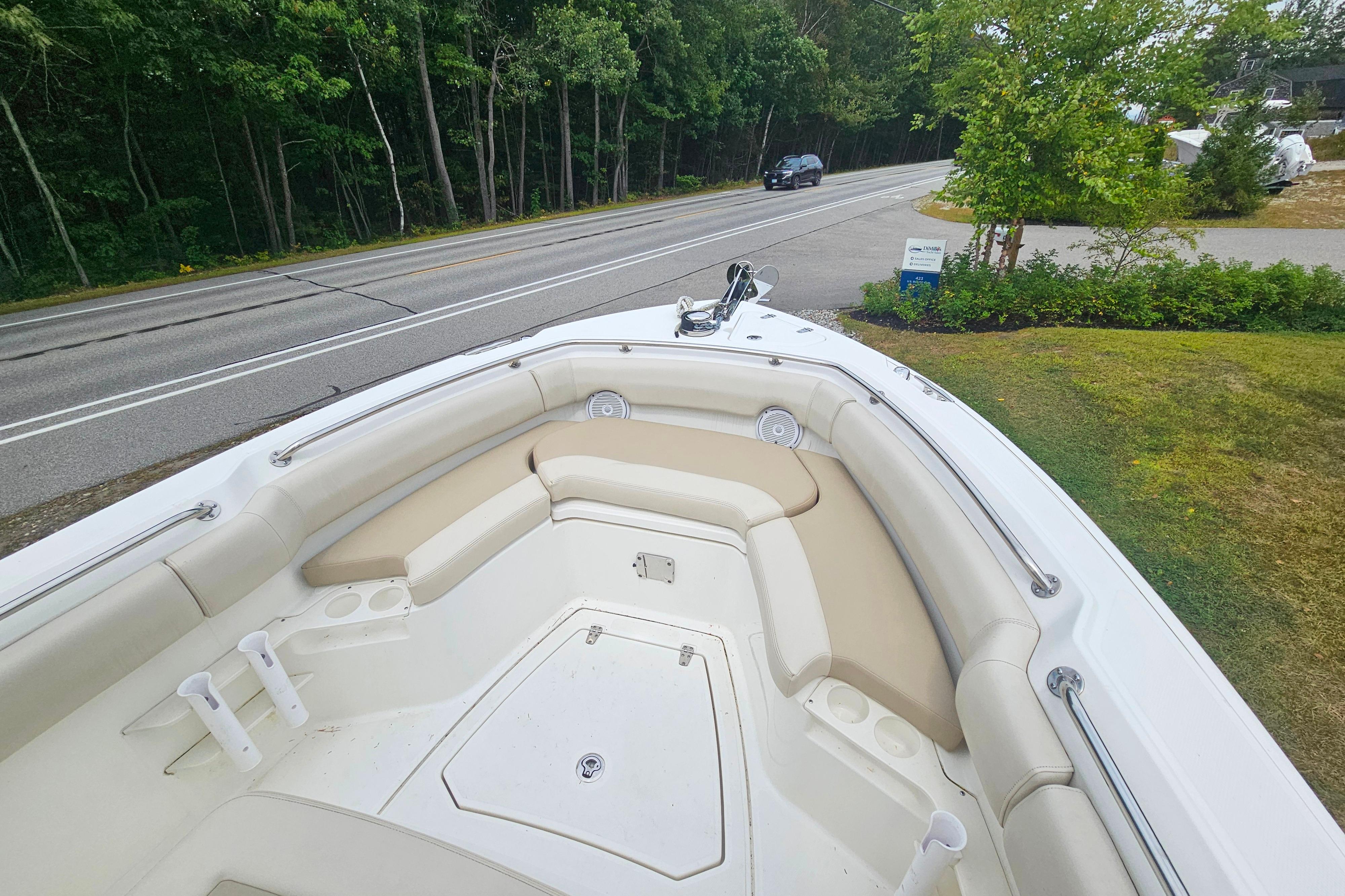 2019 Boston Whaler 230 Outrage boat with beige seating, parked near a road and greenery.