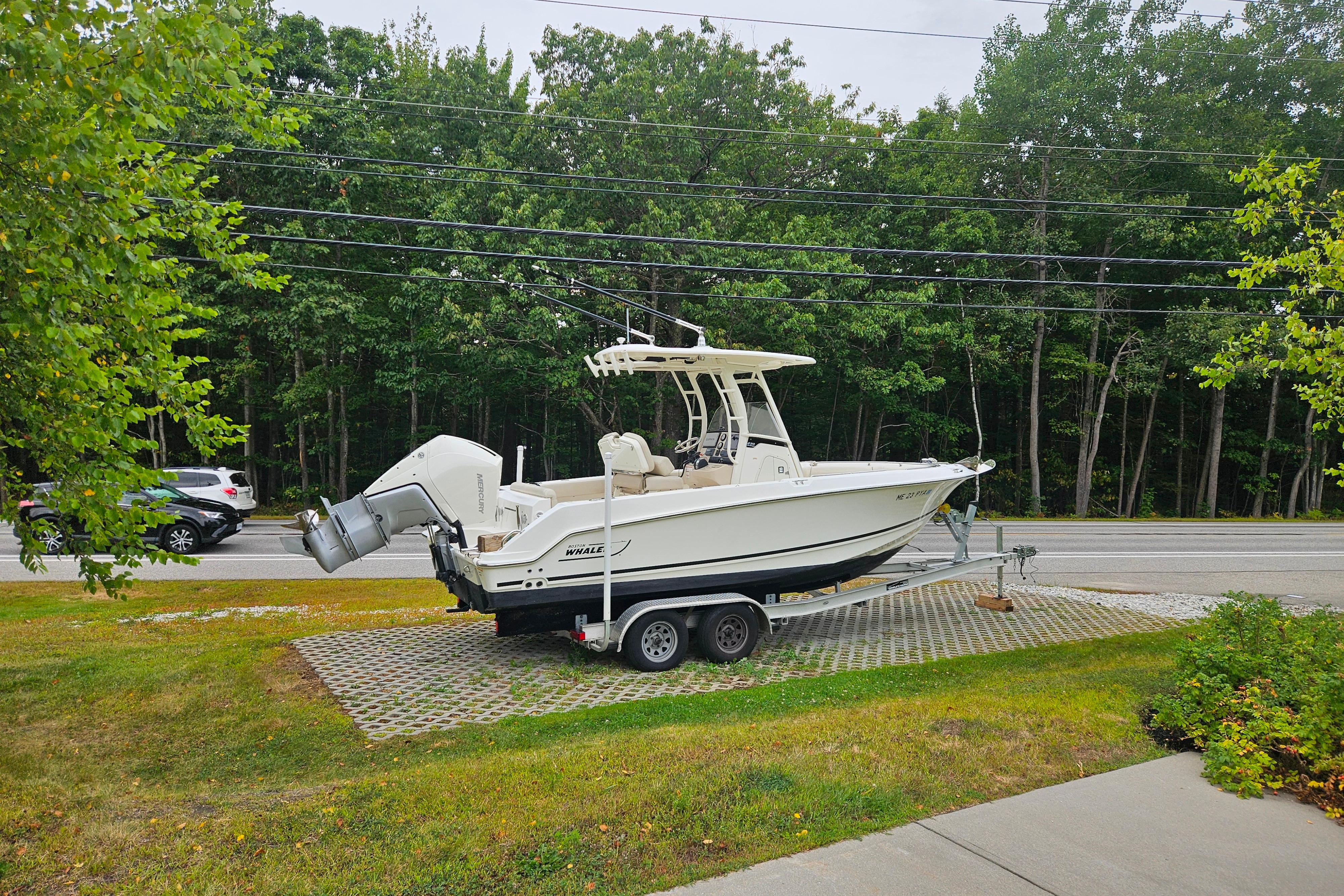 2019 Boston Whaler 230 Outrage boat on trailer, parked near a road with trees in the background.