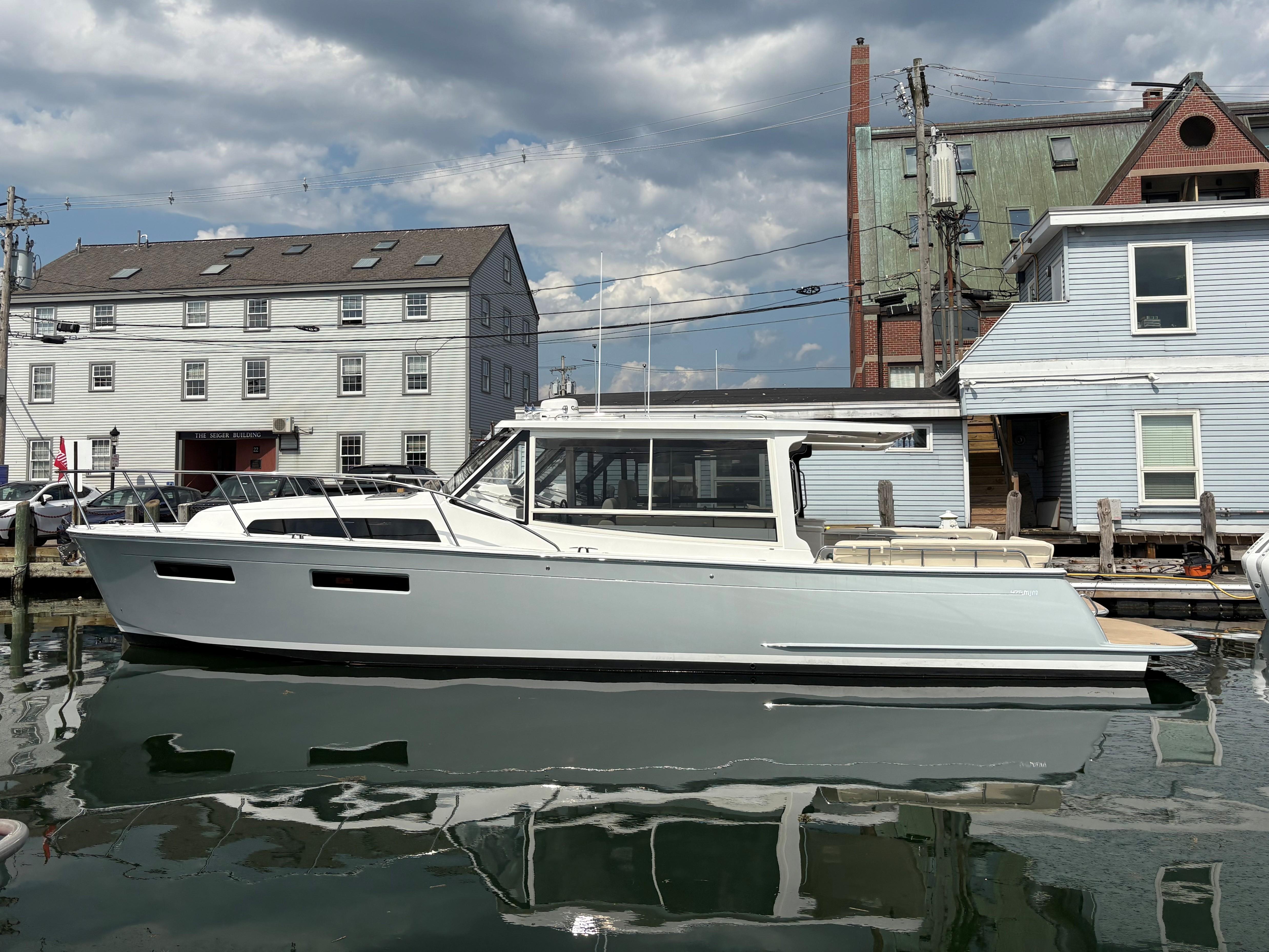 2026 MJM 47R yacht docked by historic buildings under a cloudy sky.
