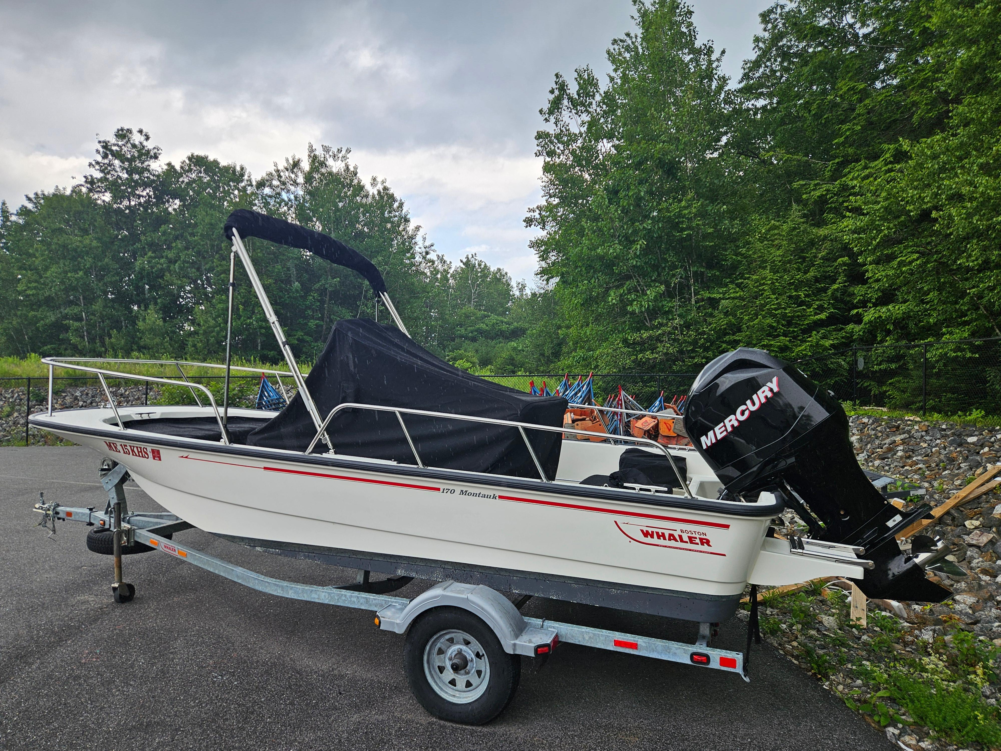 2008 Boston Whaler 170 Montauk boat on trailer, parked near lush green trees.