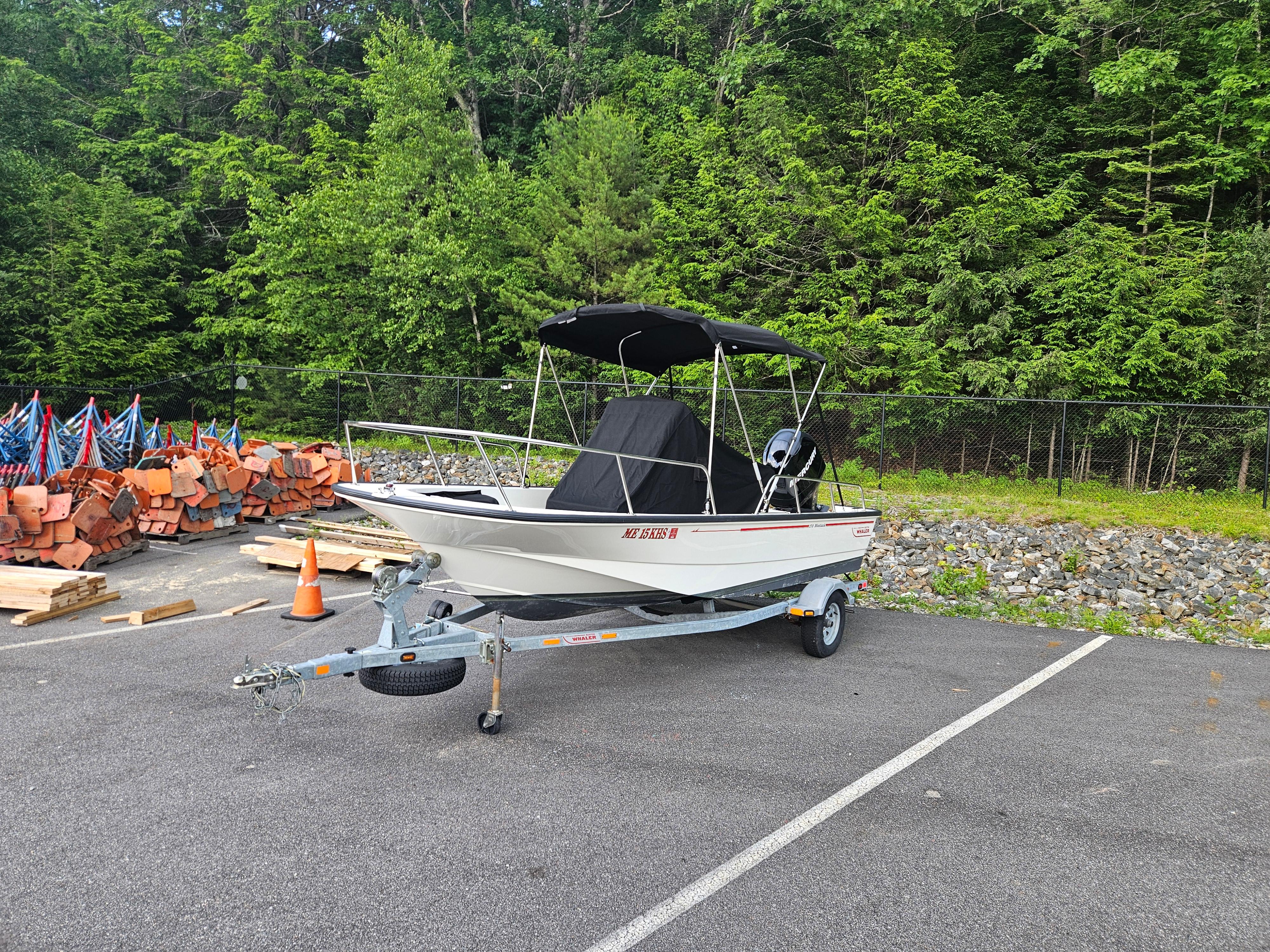 2008 Boston Whaler 170 Montauk boat on trailer in parking lot, surrounded by trees.