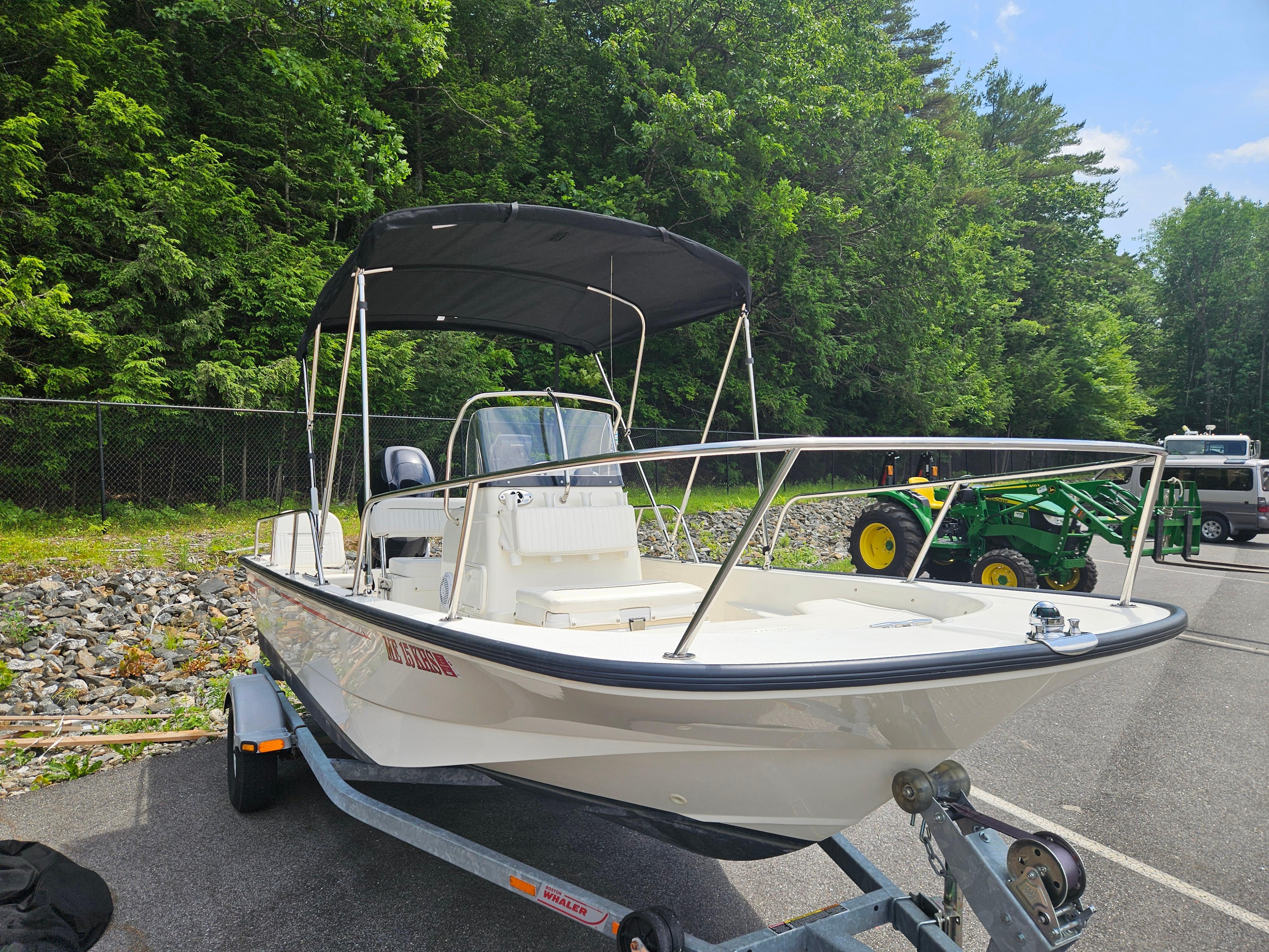 2008 Boston Whaler 170 Montauk boat on trailer, parked near trees and machinery.