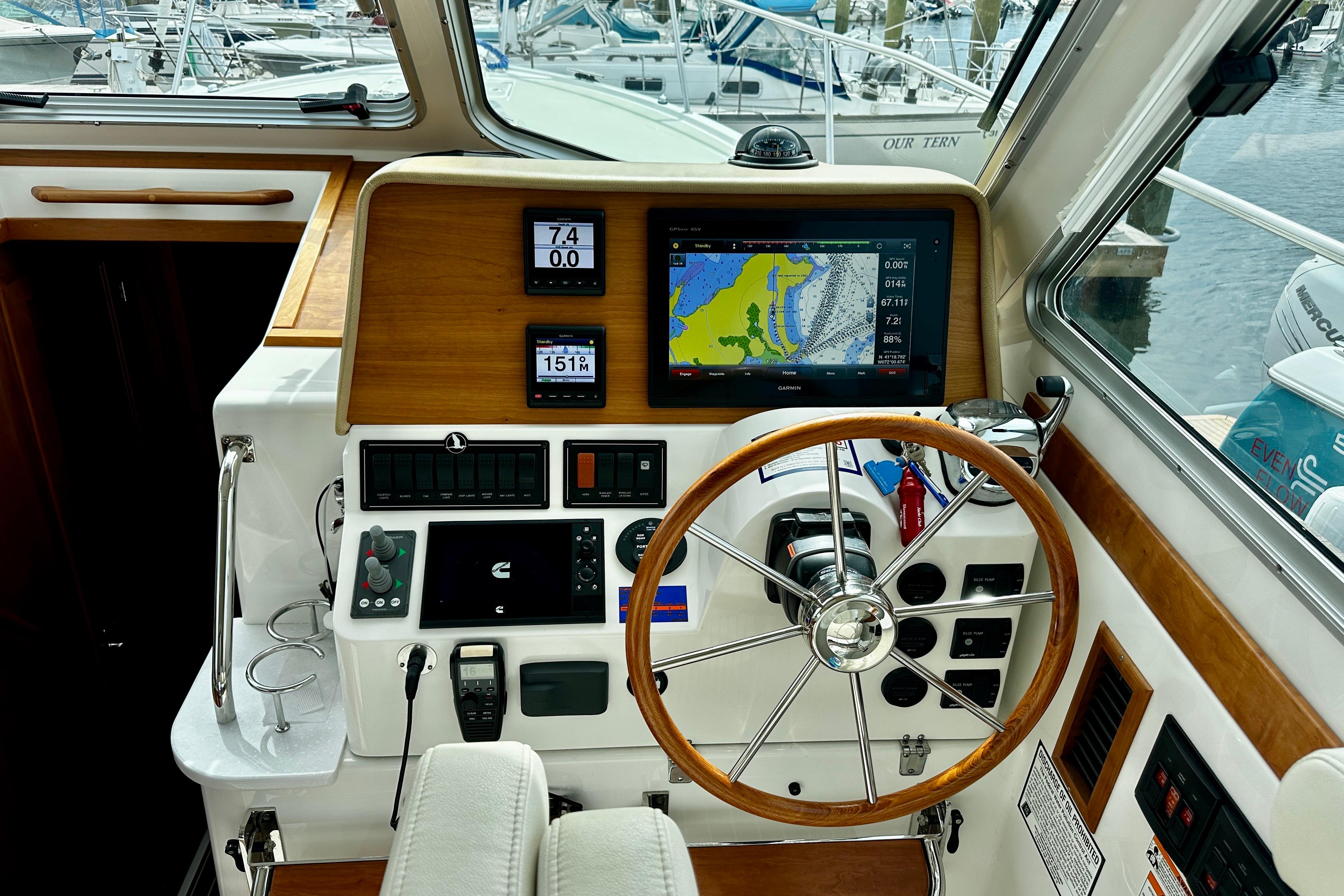2019 Back Cove 37 helm with navigation screens and wooden steering wheel in marina setting.