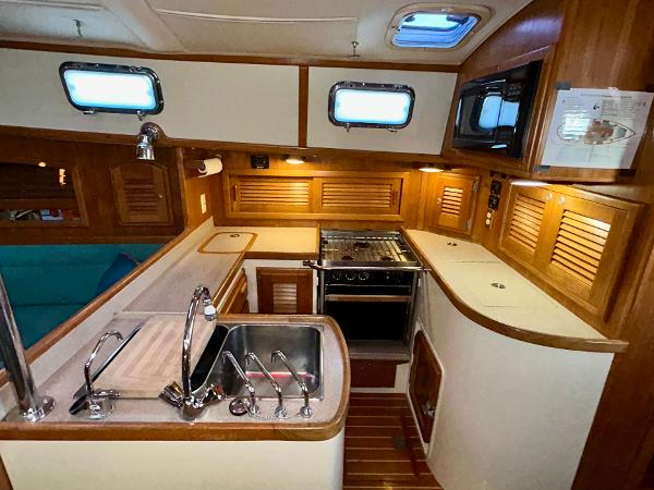 Interior of 1999 Pacific Seacraft 40 Voyagemaker yacht kitchen with wood cabinetry and stainless steel sink.