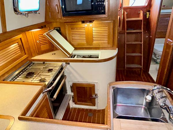 Galley kitchen in 1999 Pacific Seacraft 40 Voyagemaker yacht with wood cabinetry and stainless steel sink.