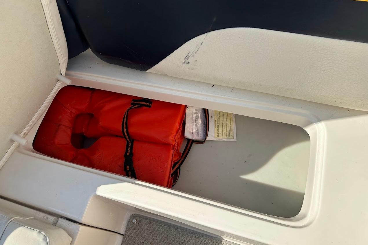 Storage compartment in a 2002 Rinker 212 Captiva boat with an orange life jacket.