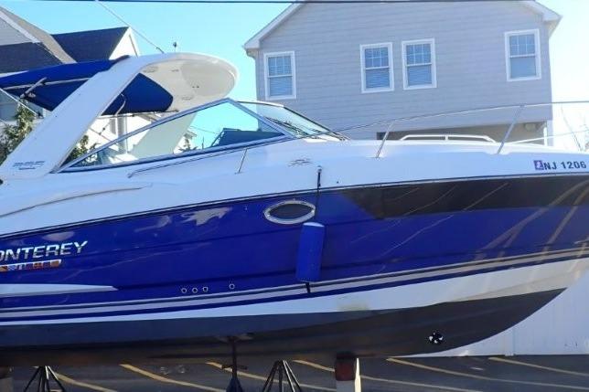 2021 Monterey 295 Sport Yacht in blue and white, displayed on stands near a house.