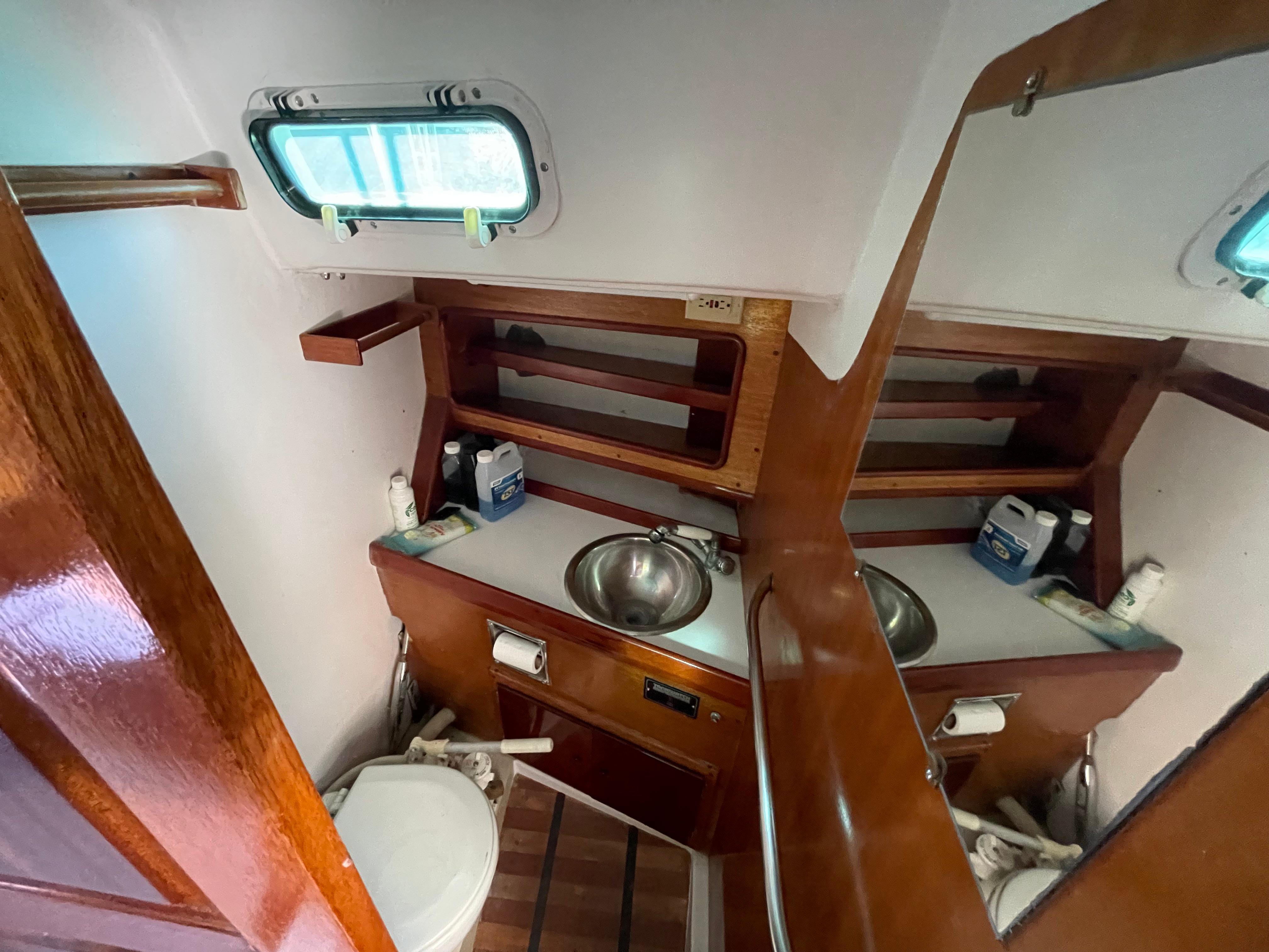 Compact wooden boat bathroom with sink, mirror, and toilet in a 1964 CAL 40 model.