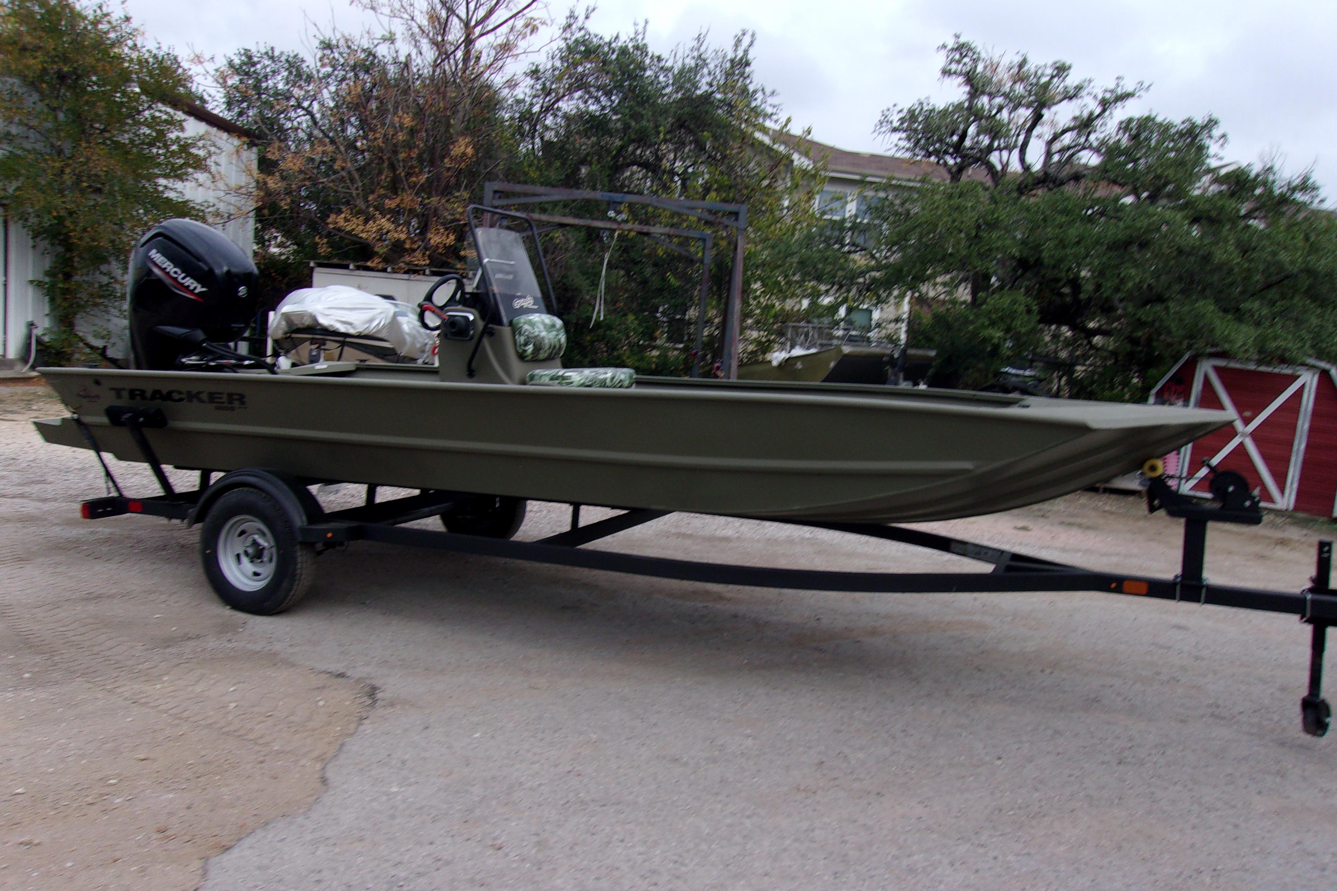 2024 Tracker Grizzly 1860 CC boat on trailer, outdoors with trees and red barn.