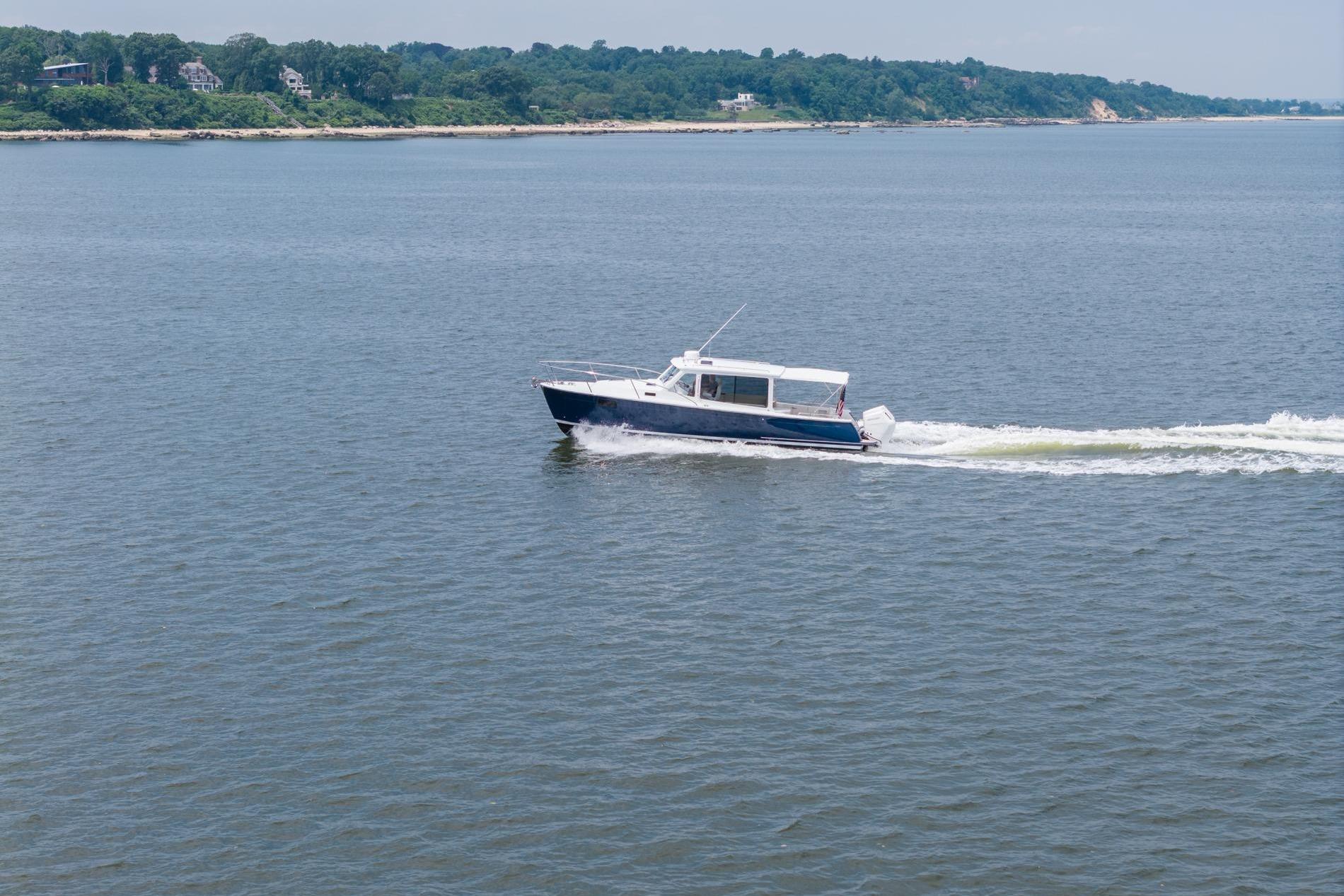 2025 MJM 35 boat cruising on a calm lake with scenic shoreline.