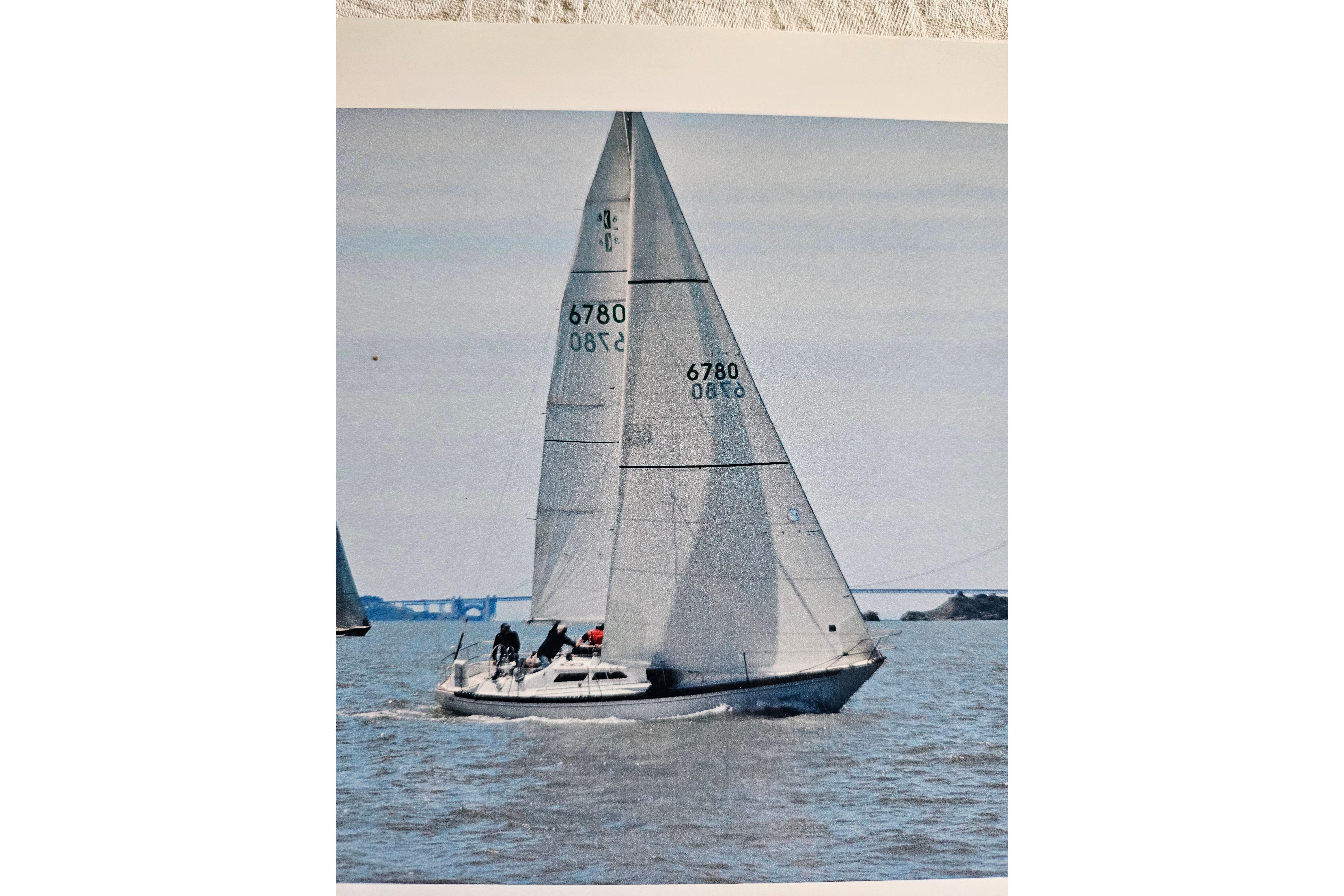1978 Islander 36 sailboat on open water, sails fully raised, with distant bridge view.