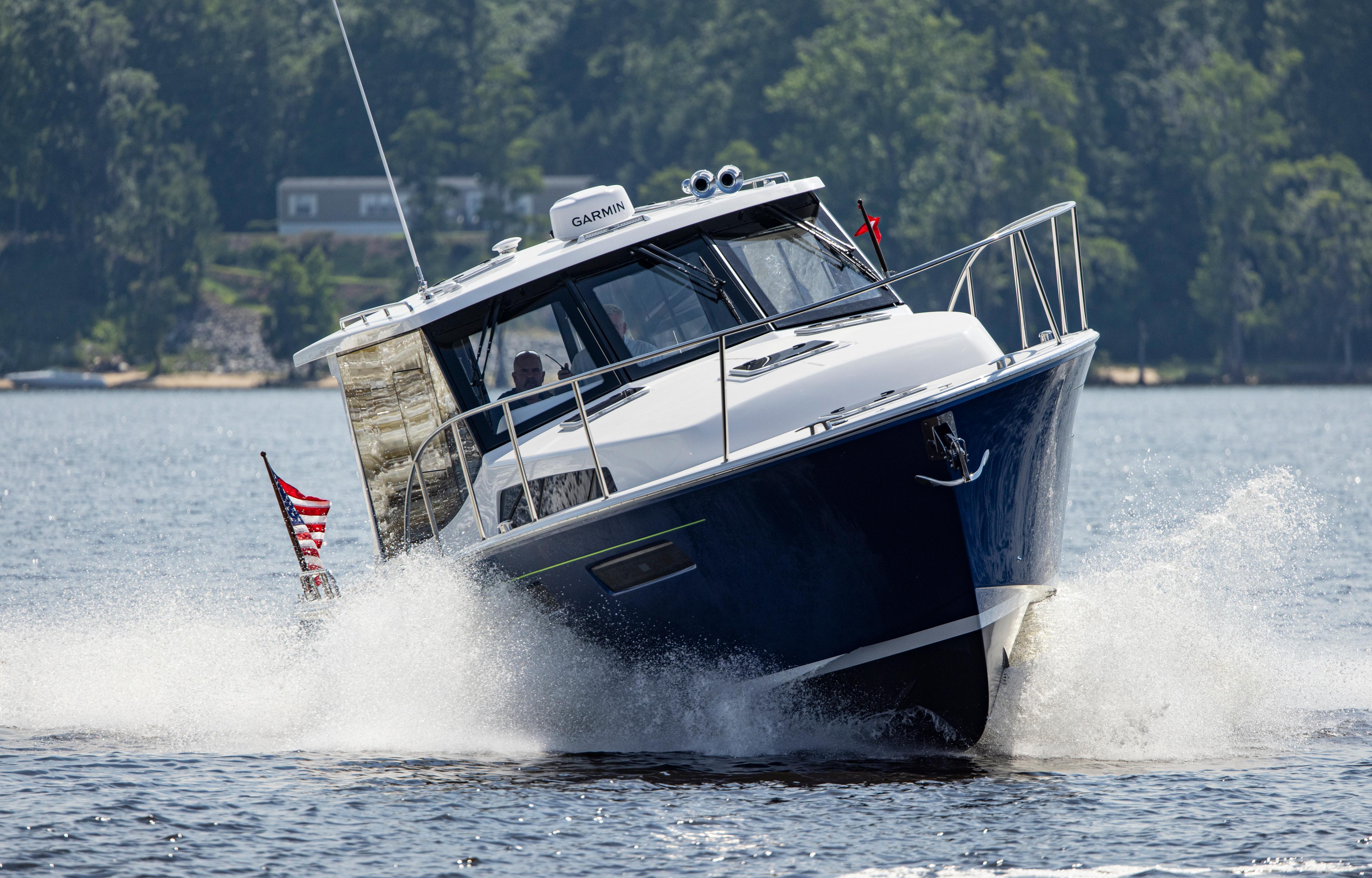 2025 MJM 42 boat cruising on a lake with American flag, surrounded by trees.