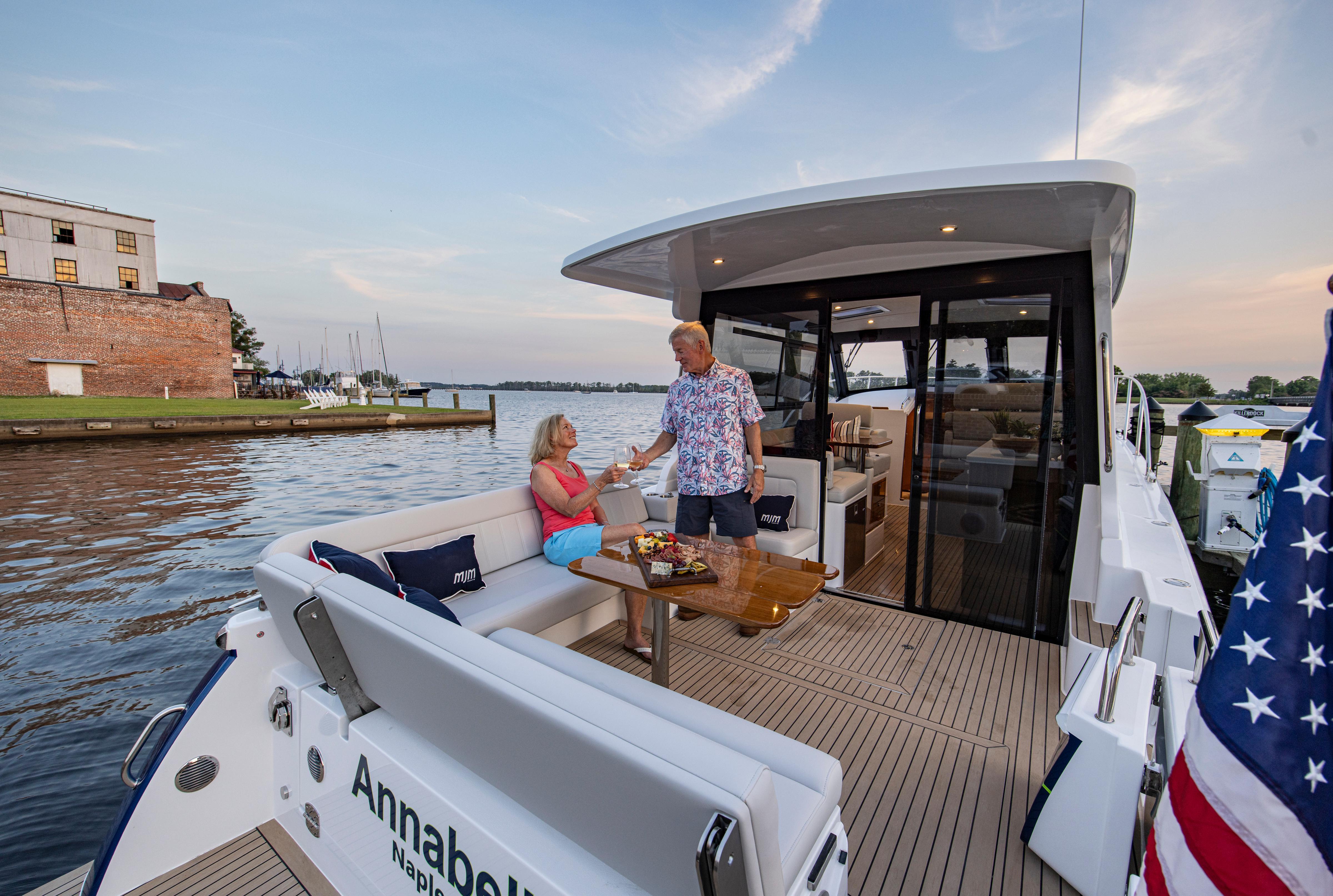 Couple enjoying drinks on a 2025 MJM 42 yacht, docked by a scenic waterfront.
