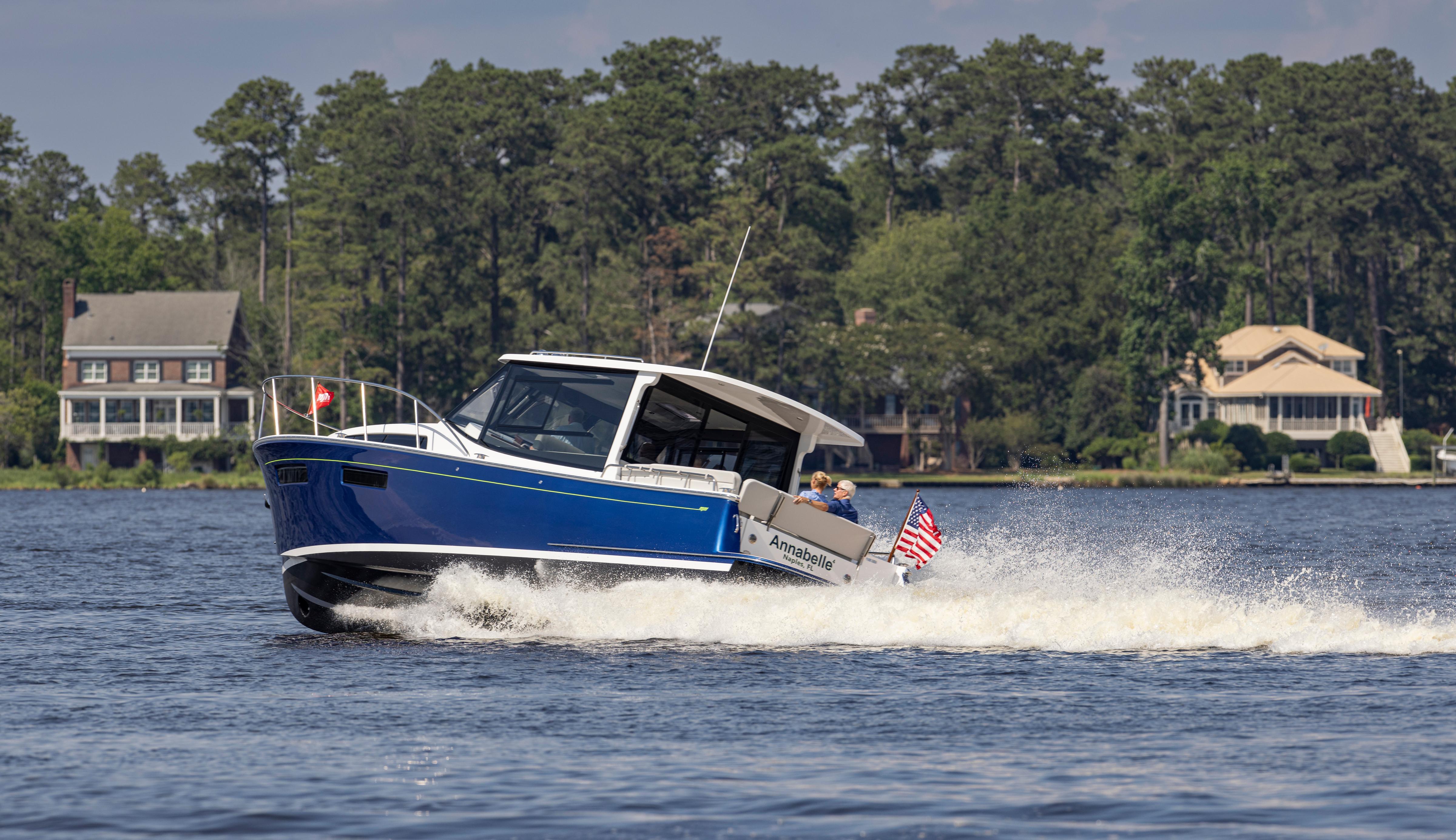 2025 MJM 42 boat cruising on a lake with houses and trees in the background.
