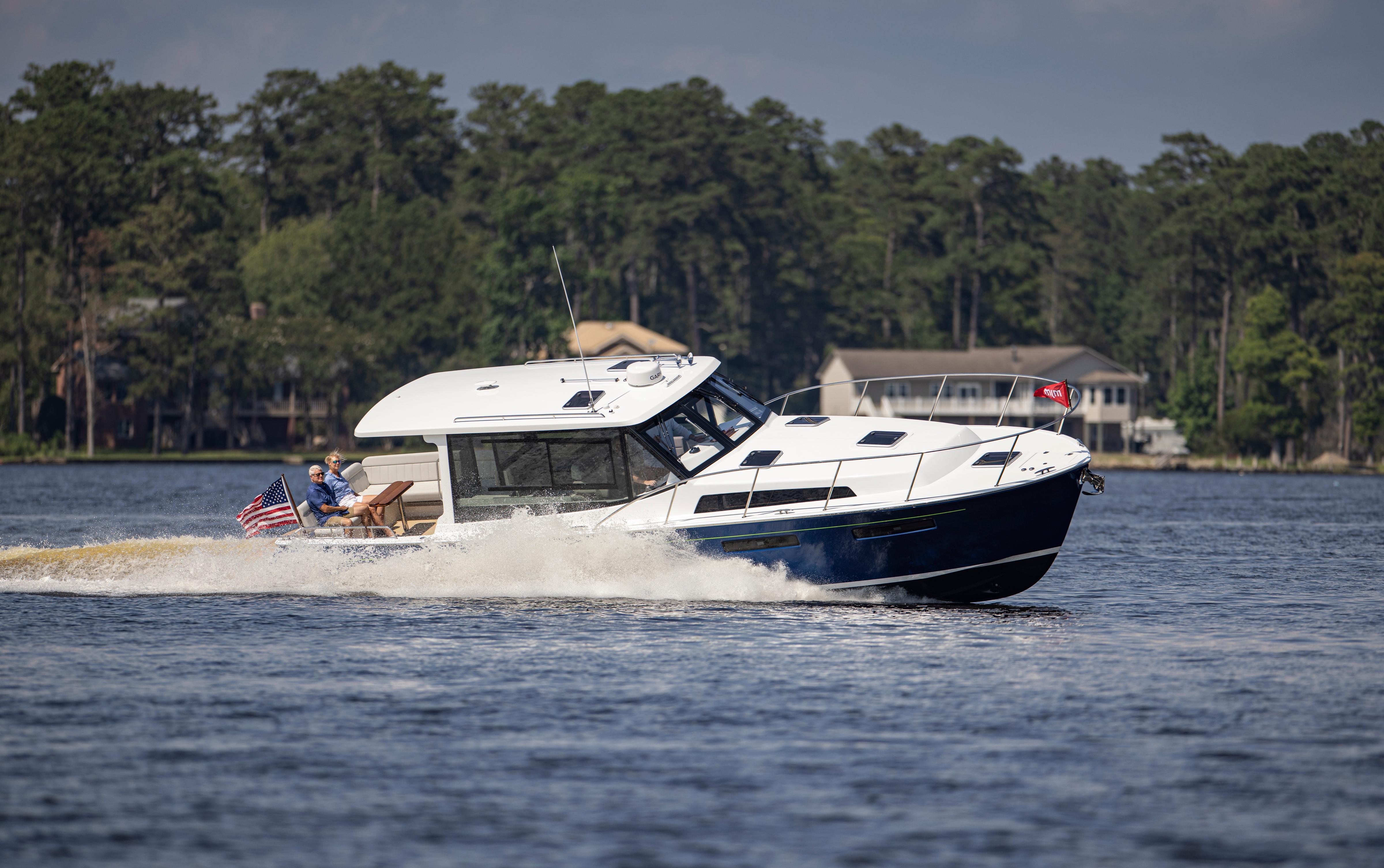 2025 MJM 42 boat cruising on a lake with passengers, surrounded by trees.