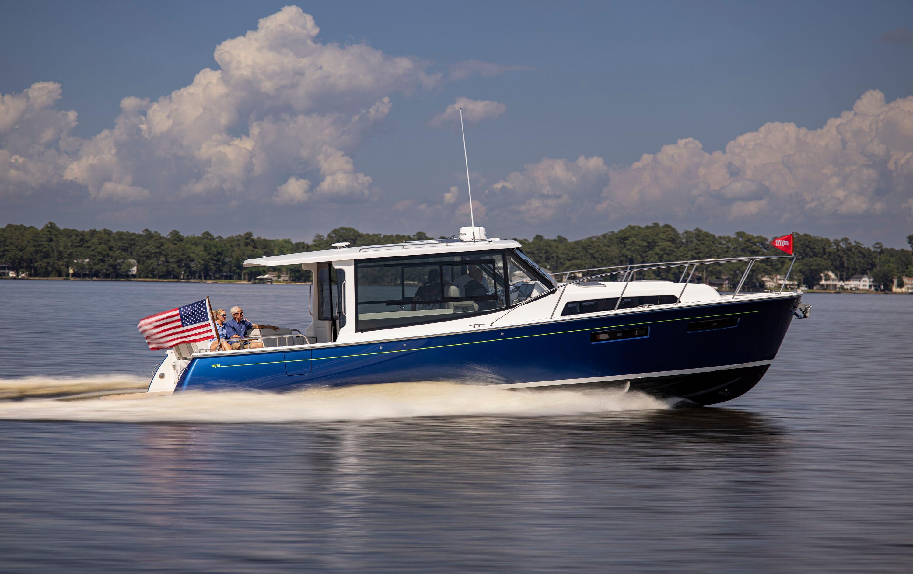 2025 MJM 42 boat cruising on a lake with American flag, clear sky background.