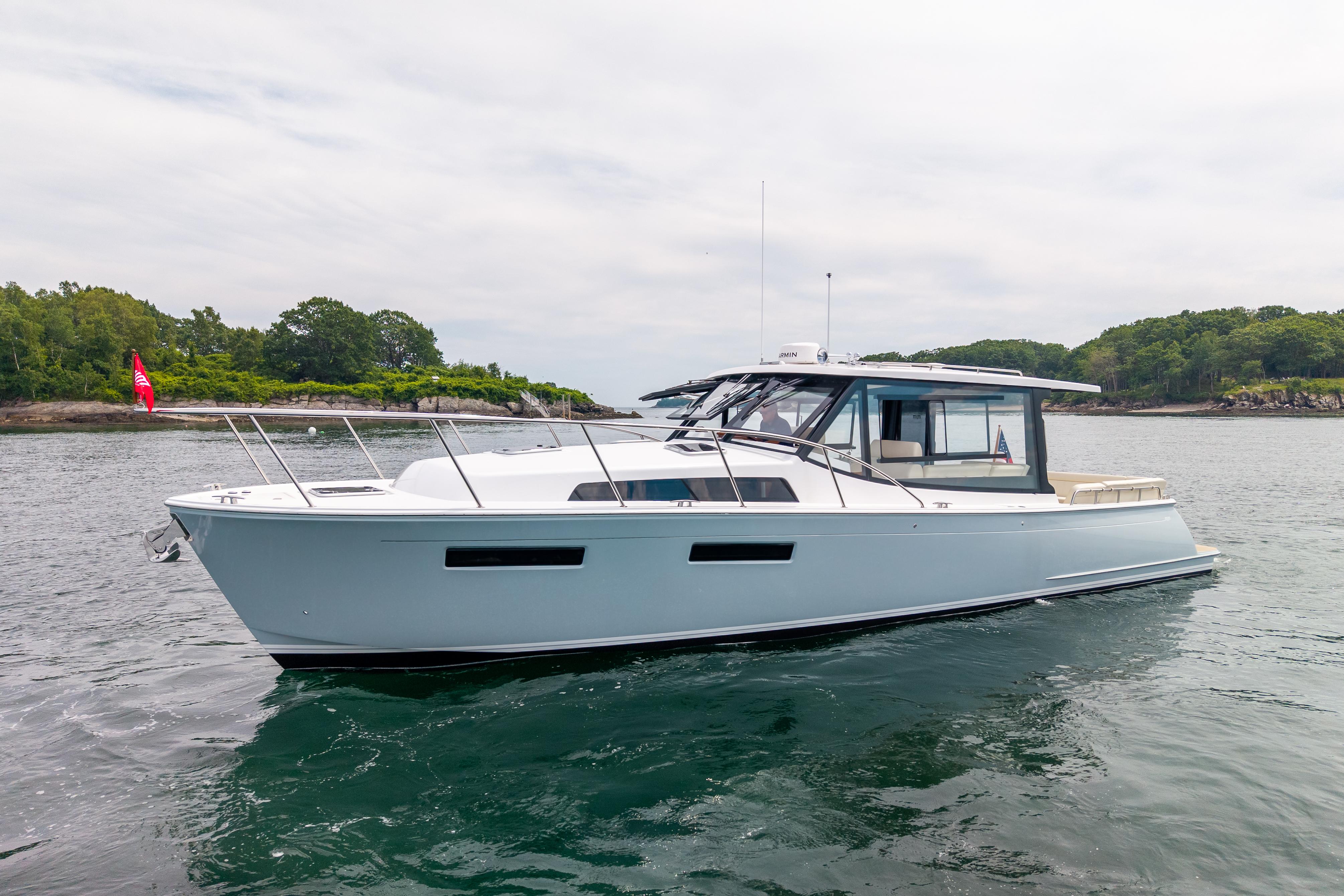 2025 MJM 42 boat cruising on calm waters near a lush, green shoreline.