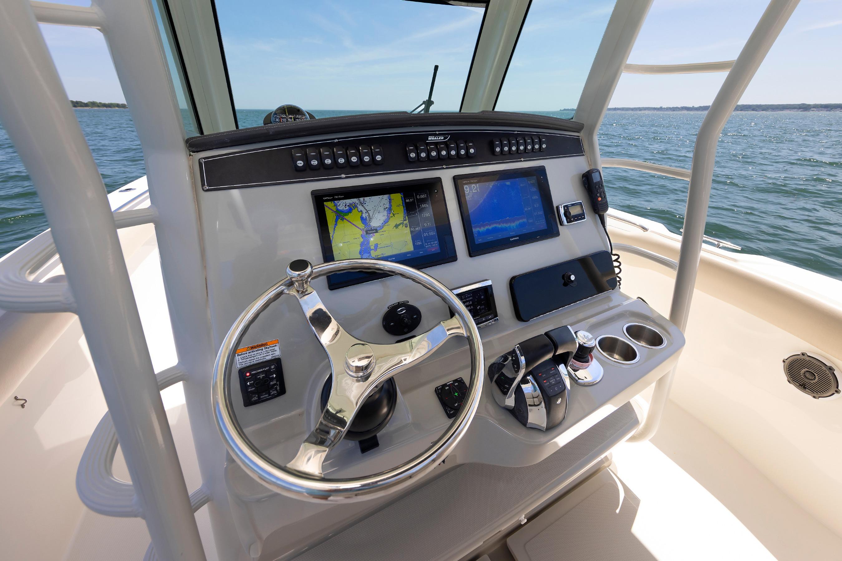 Control panel of 2016 Boston Whaler 330 Outrage boat with navigation screens and steering wheel.