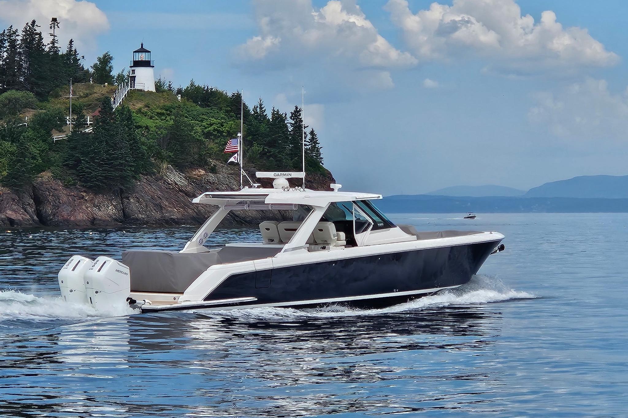 2024 Tiara Yachts 43 LS cruising near a scenic lighthouse and lush greenery.
