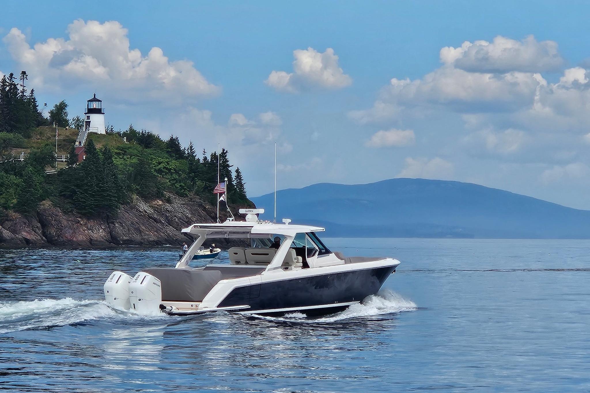2024 Tiara Yachts 43 LS cruising near a scenic lighthouse and forested coastline.