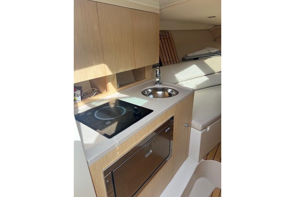 2017 Chris-Craft Corsair 32 interior kitchen with stove, sink, and wooden cabinetry.