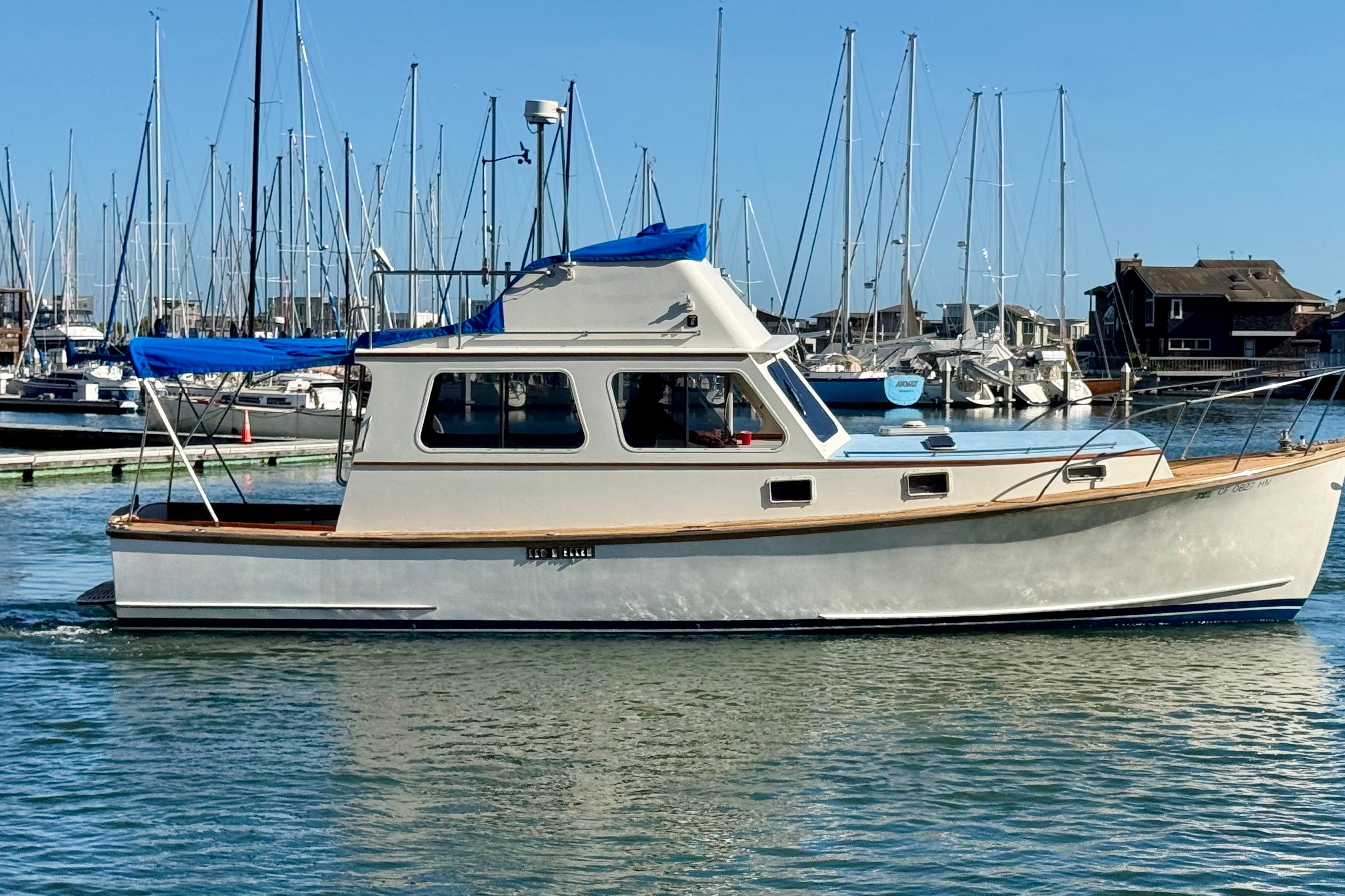 1982 Jarvis Newman Flybridge Cruiser in marina, surrounded by sailboats, under clear blue sky.