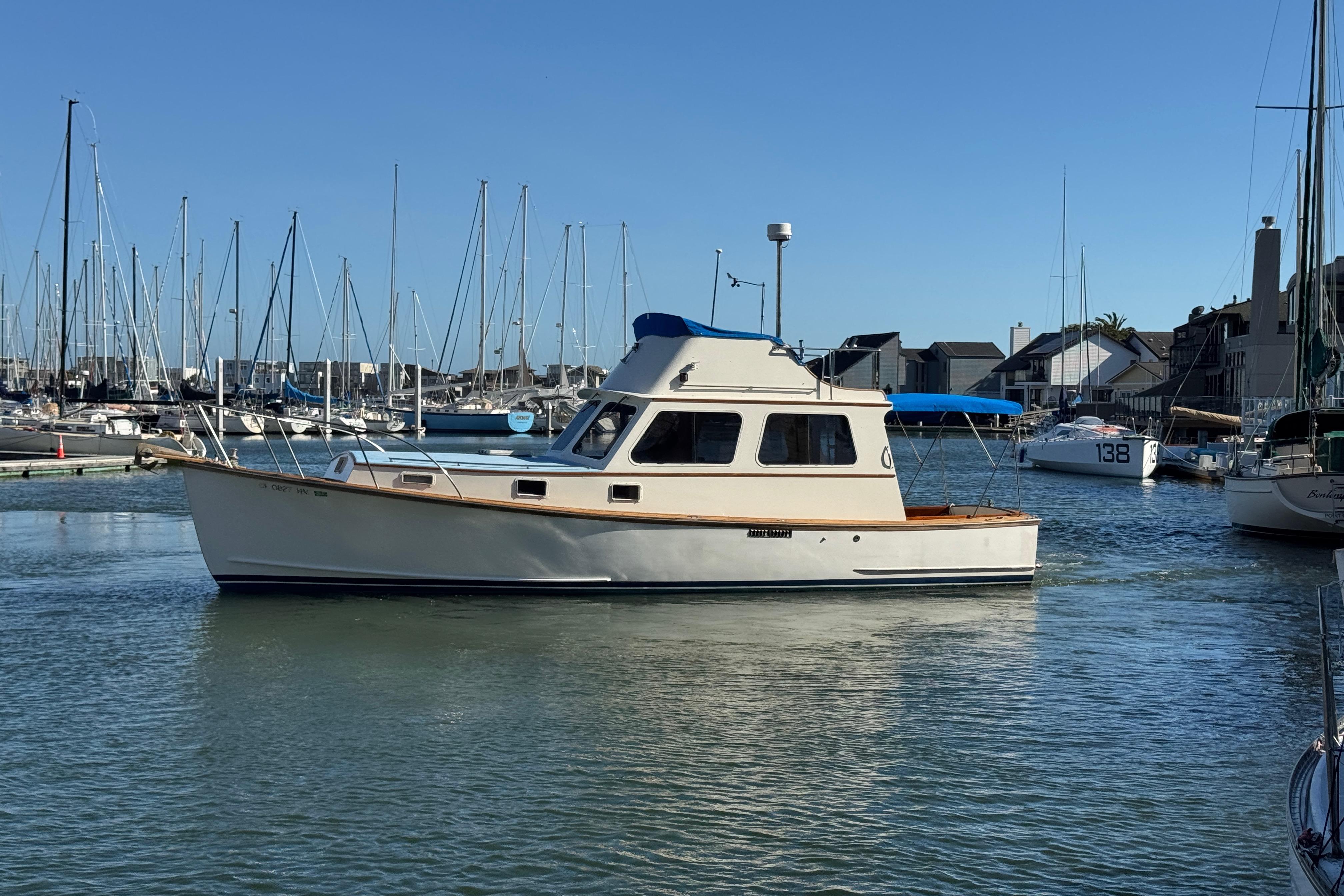 1982 Jarvis Newman Flybridge Cruiser in marina, surrounded by sailboats under clear blue sky.