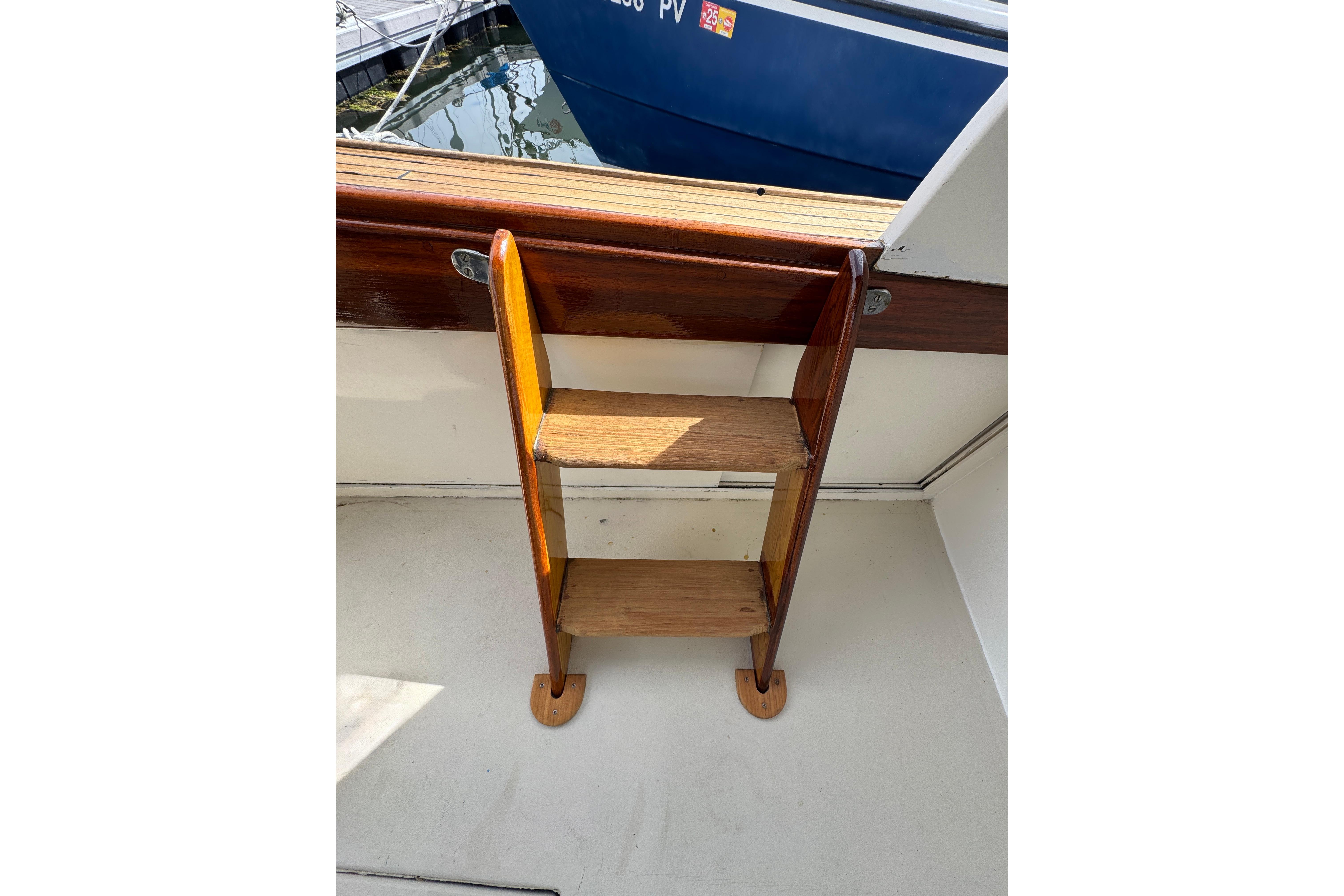 Wooden ladder on 1982 Jarvis Newman Flybridge Cruiser, docked near a blue boat.