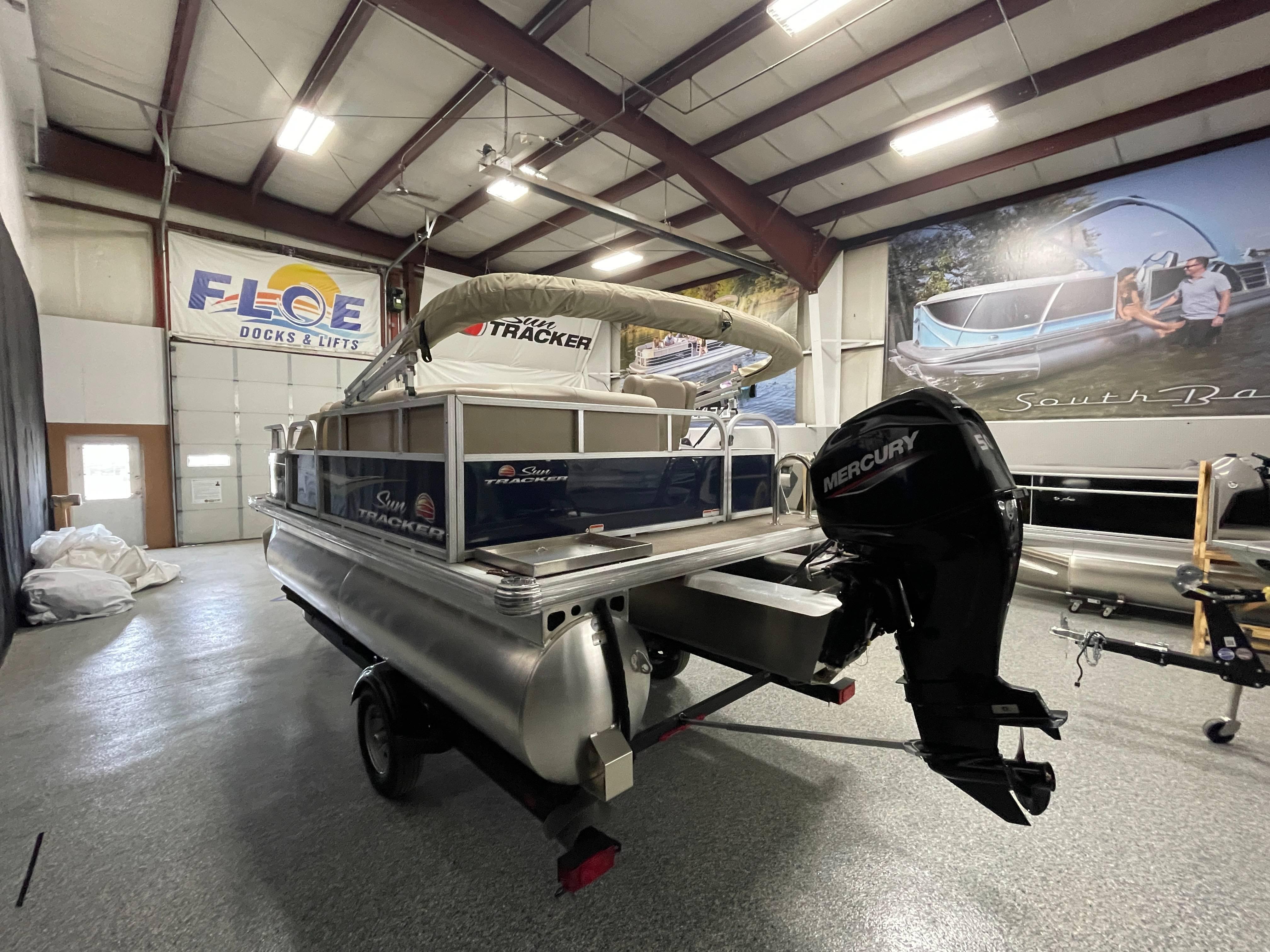 2025 Sun Tracker Bass Buggy 16 XL Select pontoon boat in showroom with Mercury outboard motor.