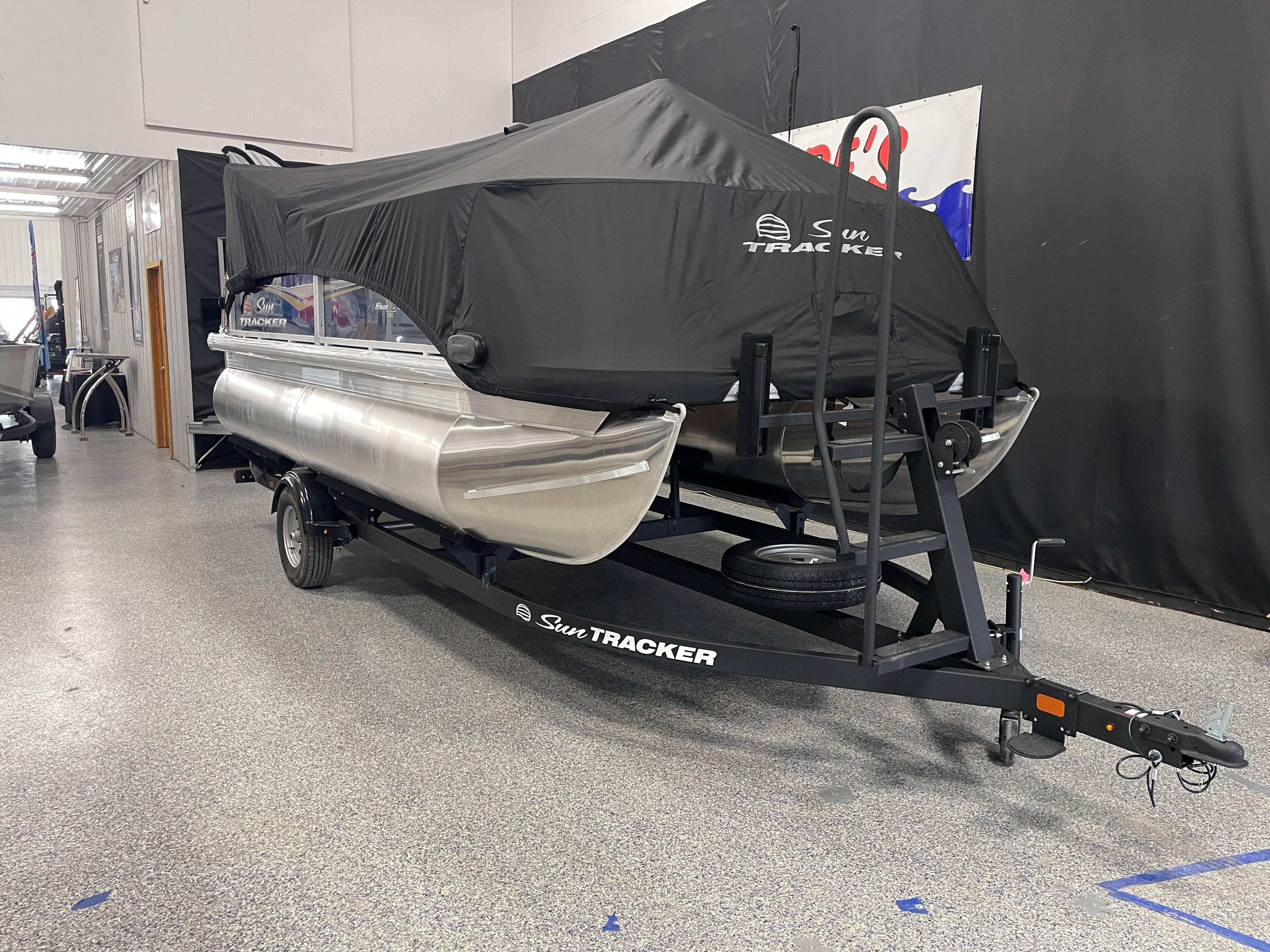 2025 Sun Tracker Bass Buggy 16 XL Select pontoon boat on trailer, covered and parked indoors.