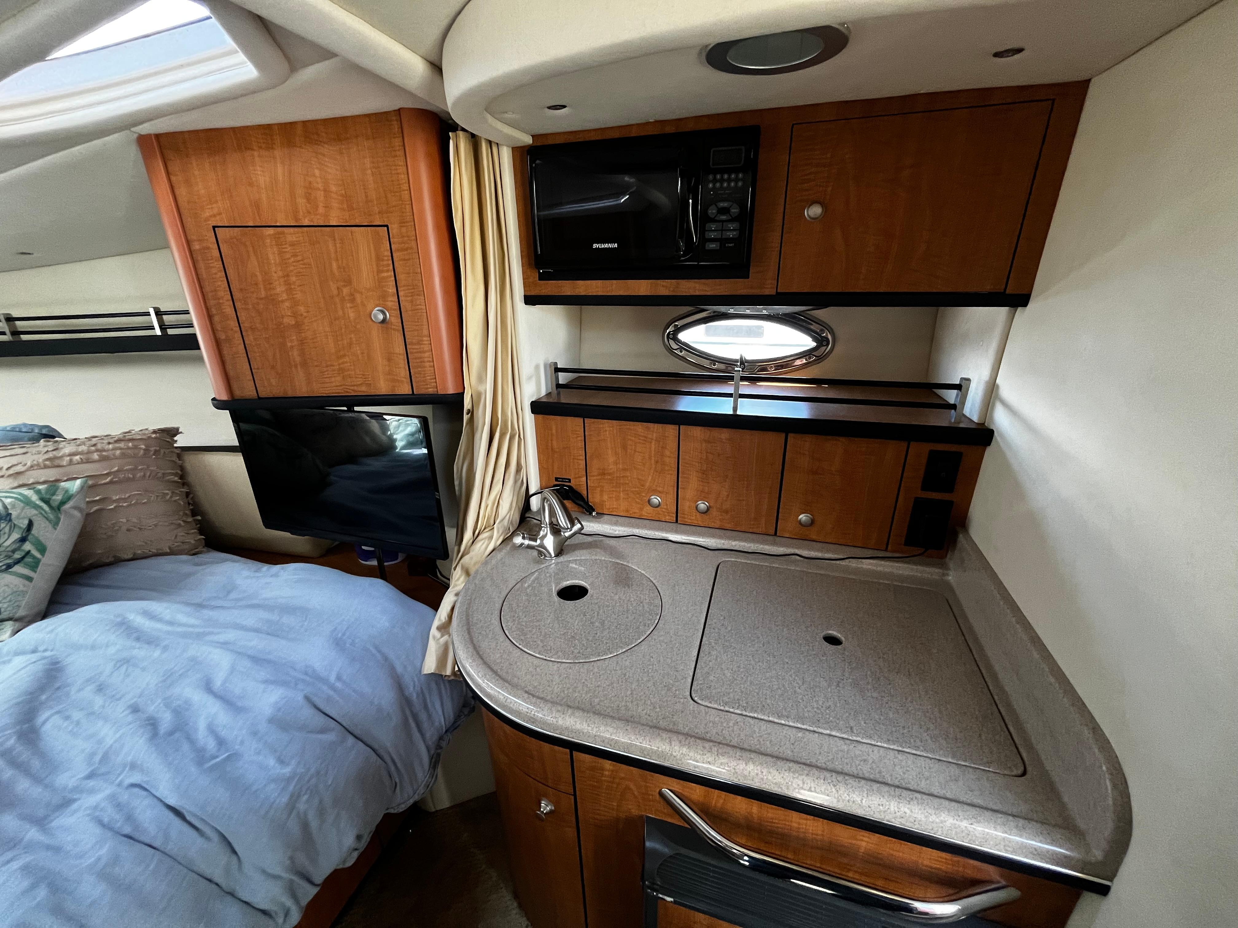 2006 Sea Ray 290 Sundancer interior with kitchenette and bed, featuring wood cabinetry and modern amenities.