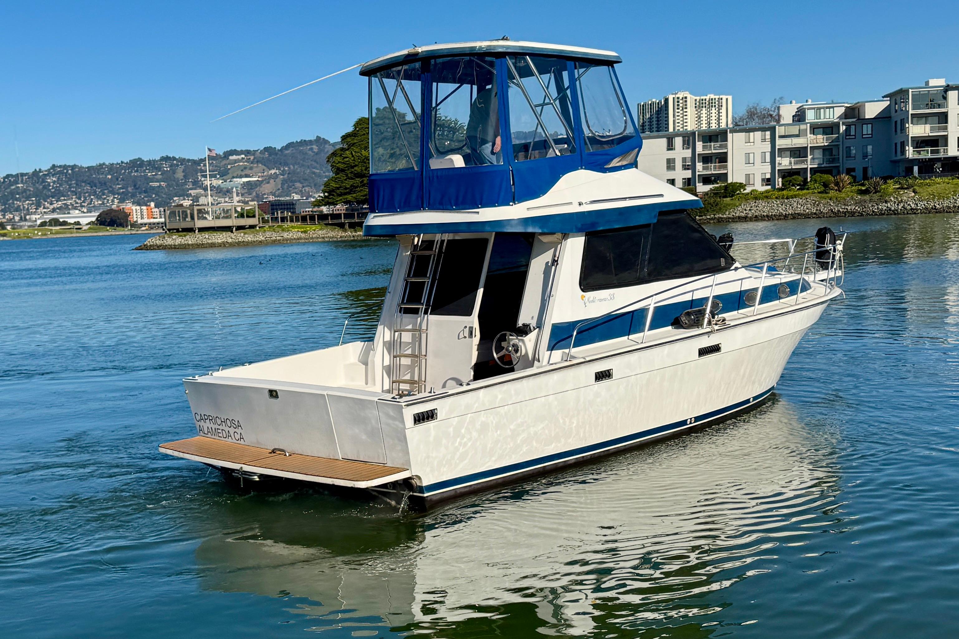 1989 Mediterranean 38 yacht on calm water near urban shoreline.