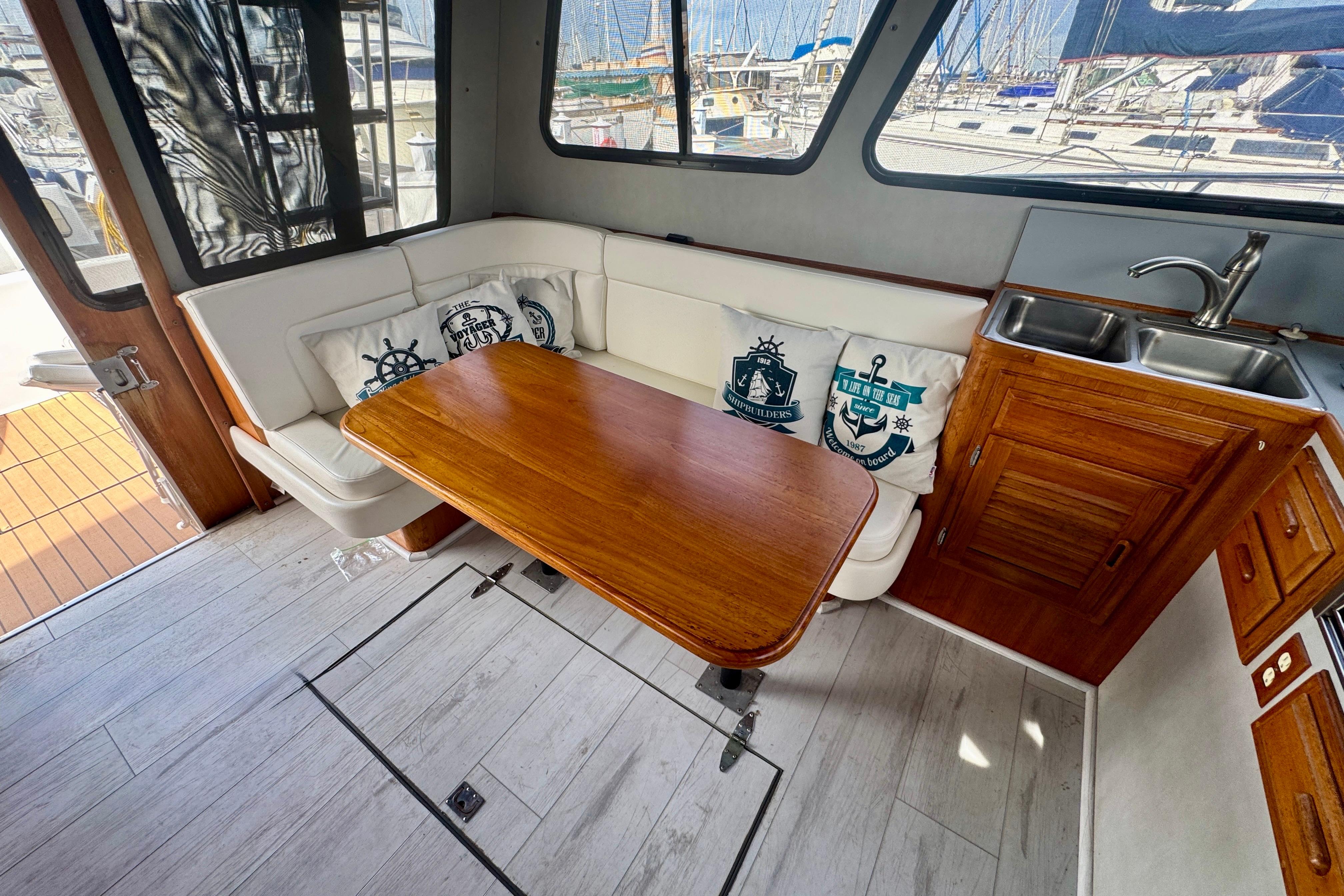 Cozy interior of 1989 Mediterranean 38 yacht with wooden table, white seating, and kitchenette.